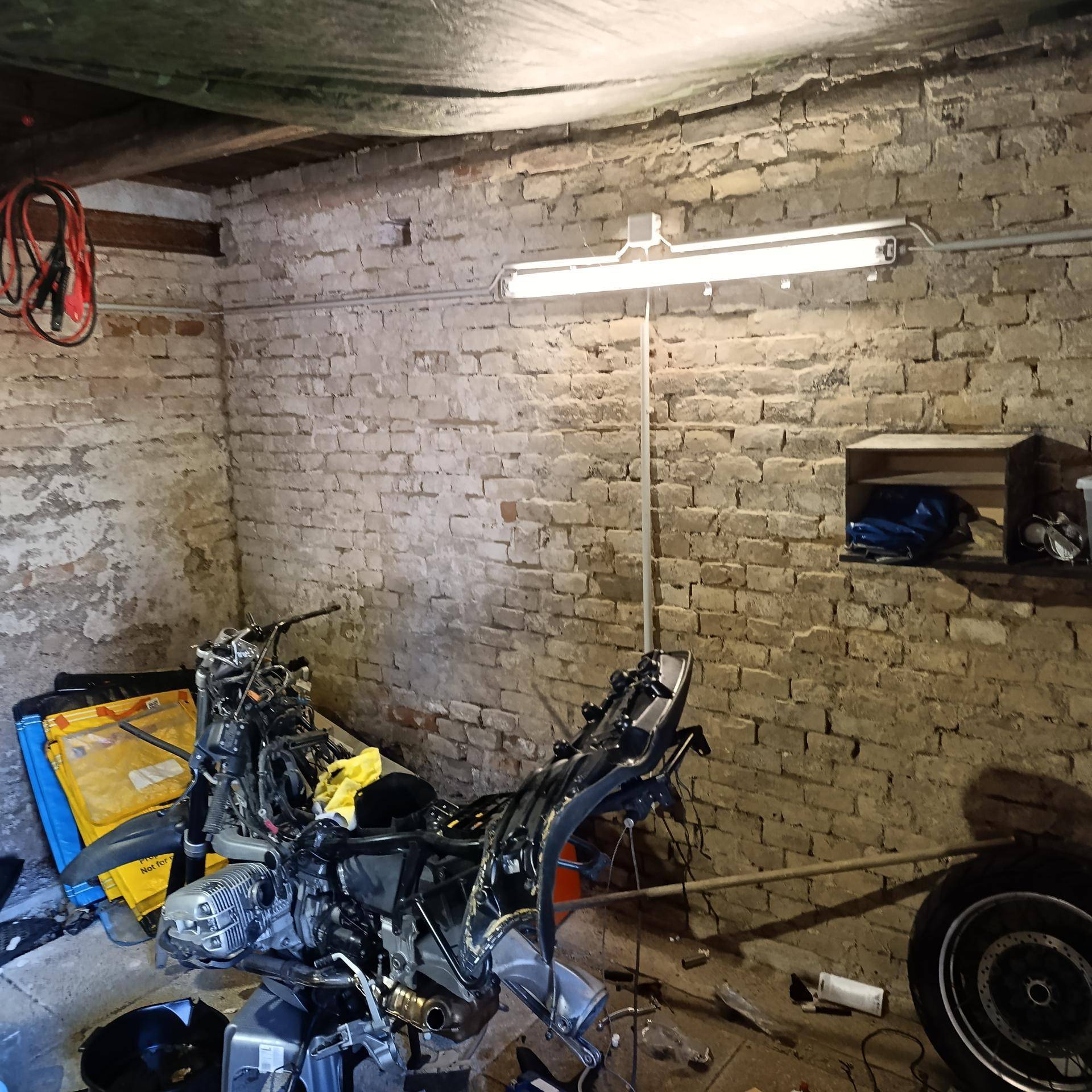 Innenansicht einer Werkstatt mit unverputzten Ziegelwänden, einem Motorradrahmen und einer Leuchtstofflampe an der Decke.
