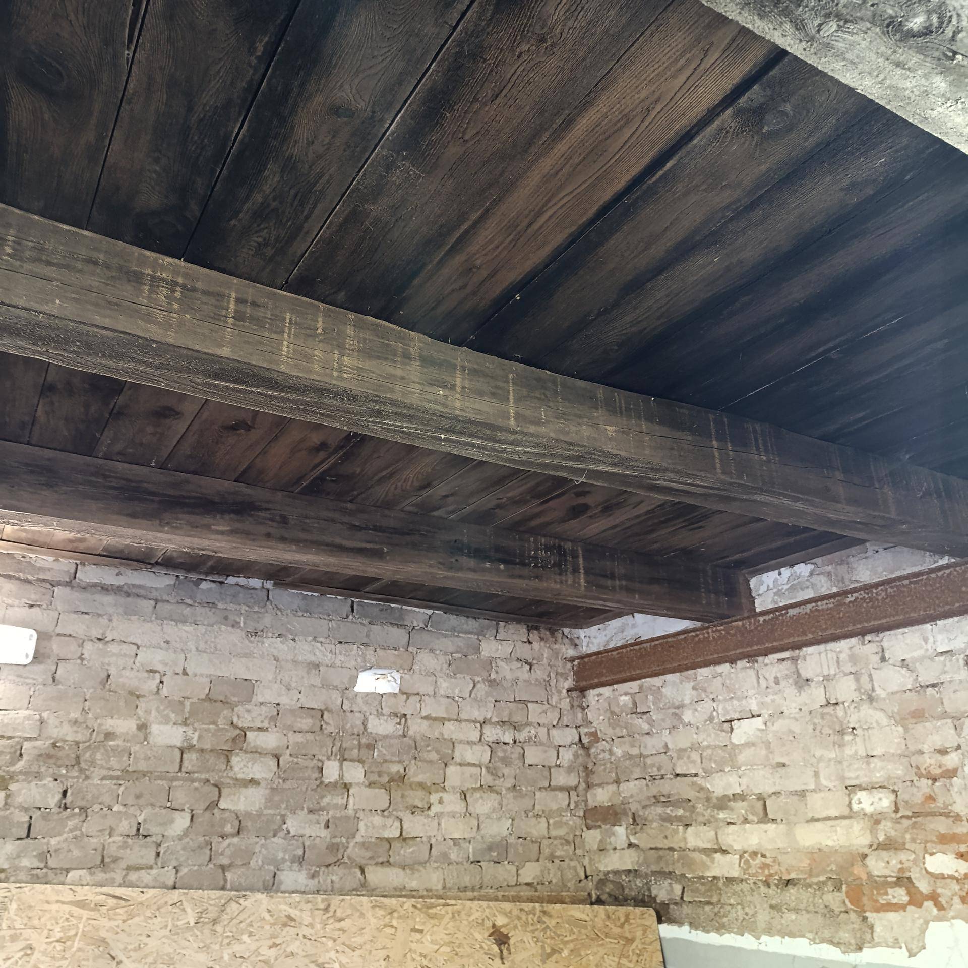 Blick auf die Holzbalkendecke und die unverputzten Ziegelwände eines rustikalen Innenraums mit hoher Decke.