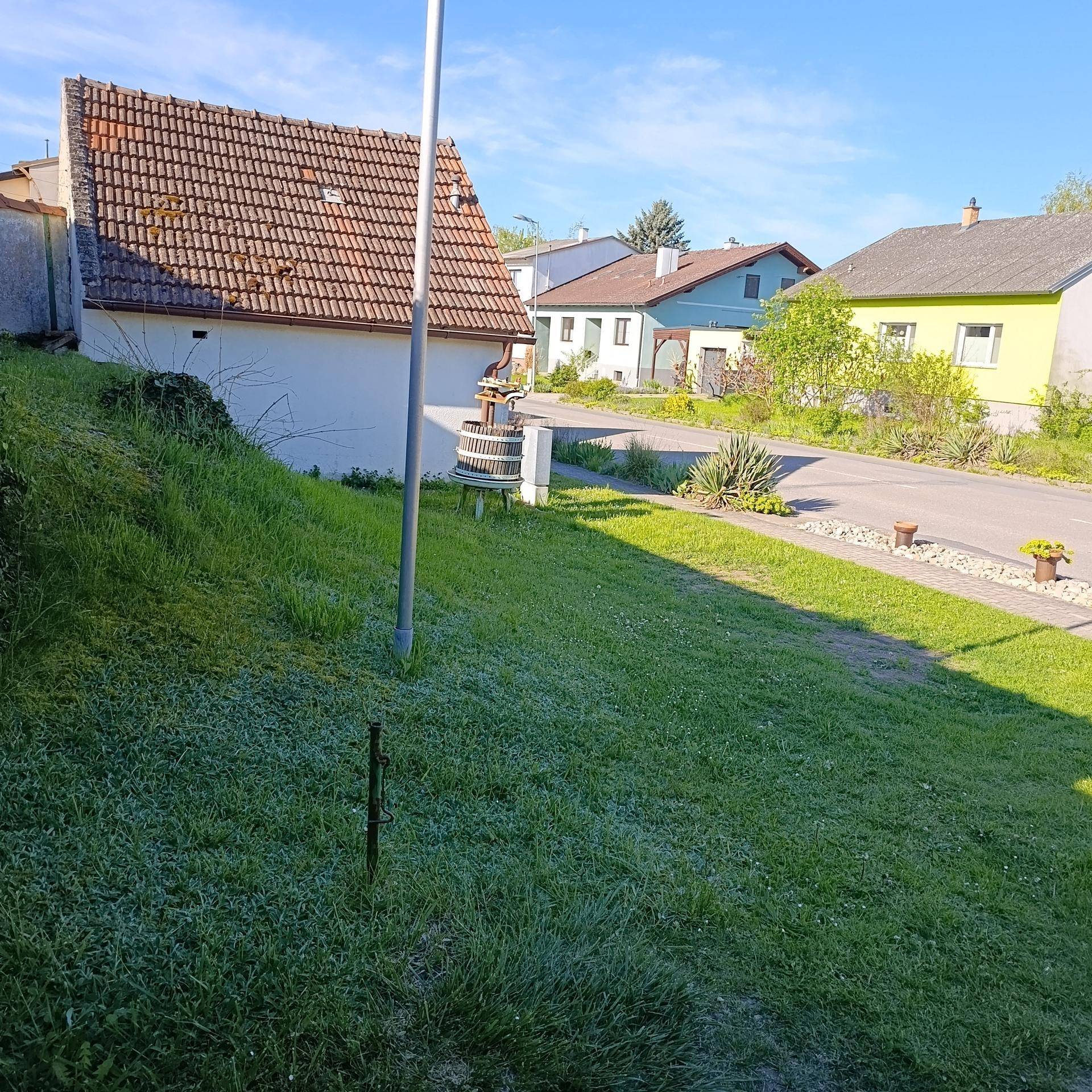 Eine grüne Wiese mit einem Mast und weiteren Wohnhäusern im Hintergrund unter blauem Himmel und Sonnenschein.
