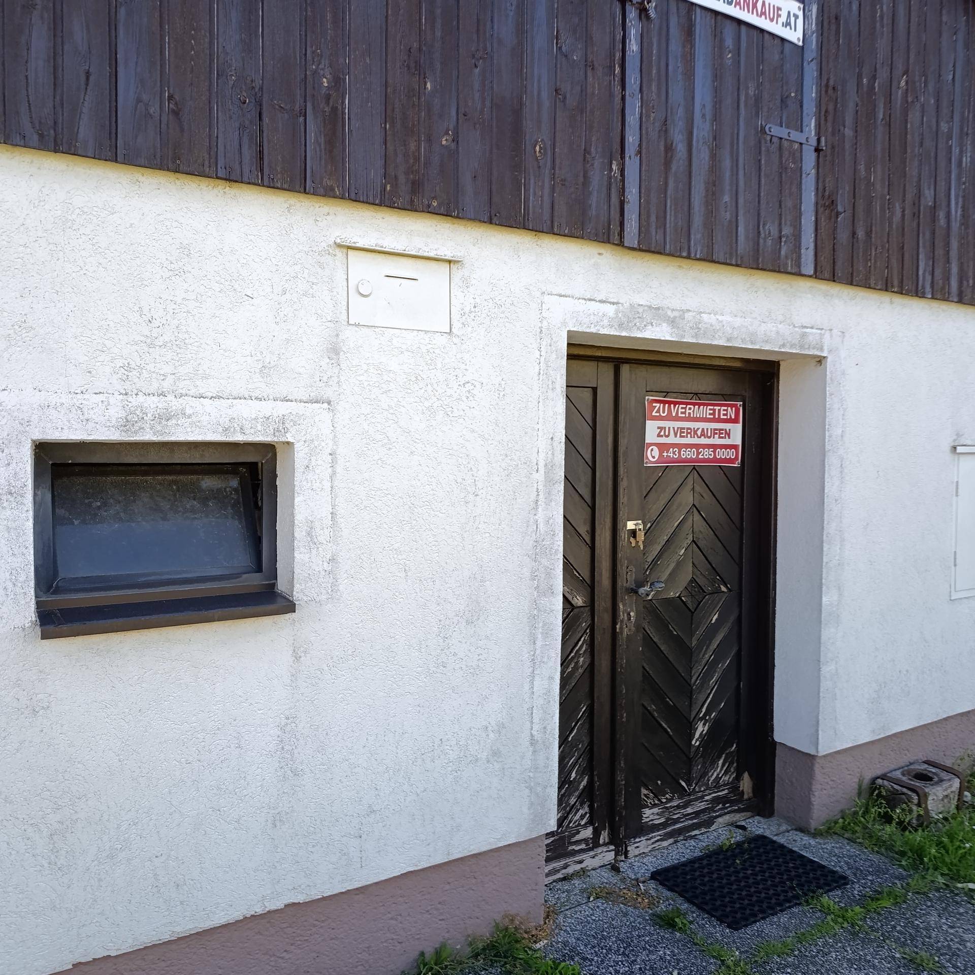 Detailansicht des Eingangs mit Holztüren, einem kleinen Fenster und einem roten "Zu Vermieten" Schild an der Fassade.