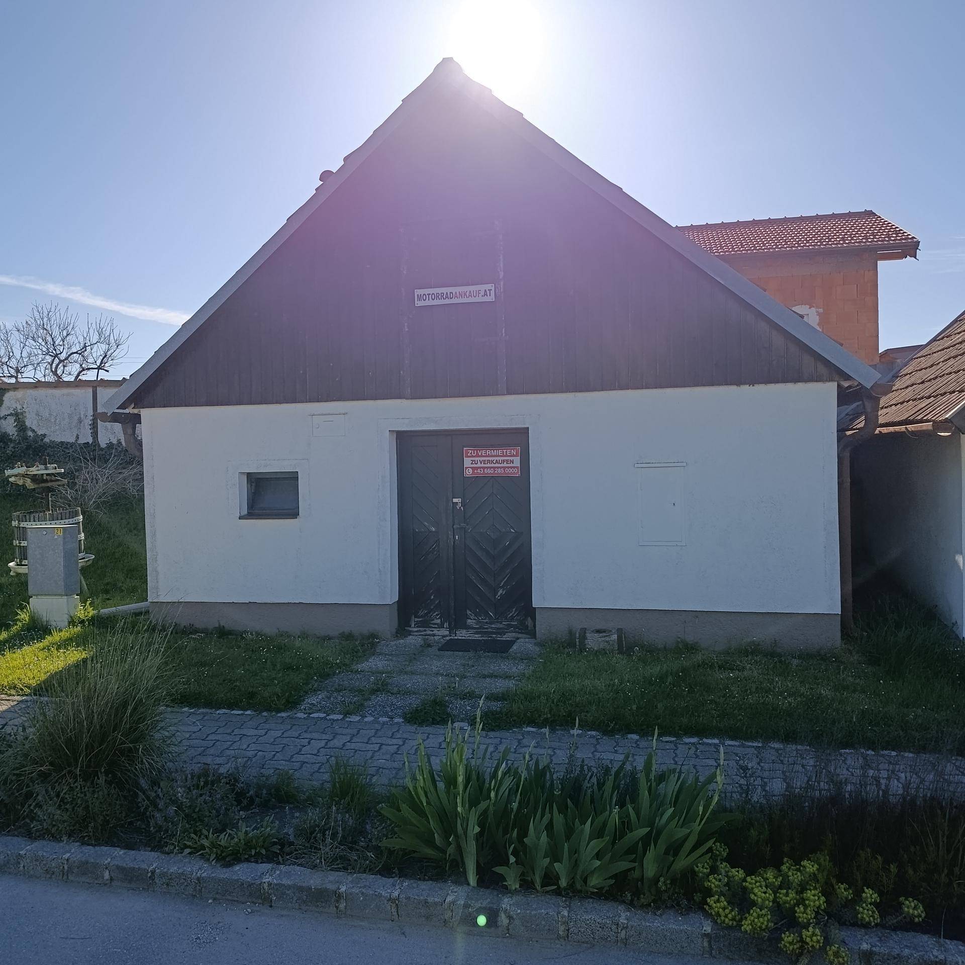 Frontansicht eines Gebäudes mit weißer Fassade und dunklem Holzdach unter strahlendem Sonnenschein.