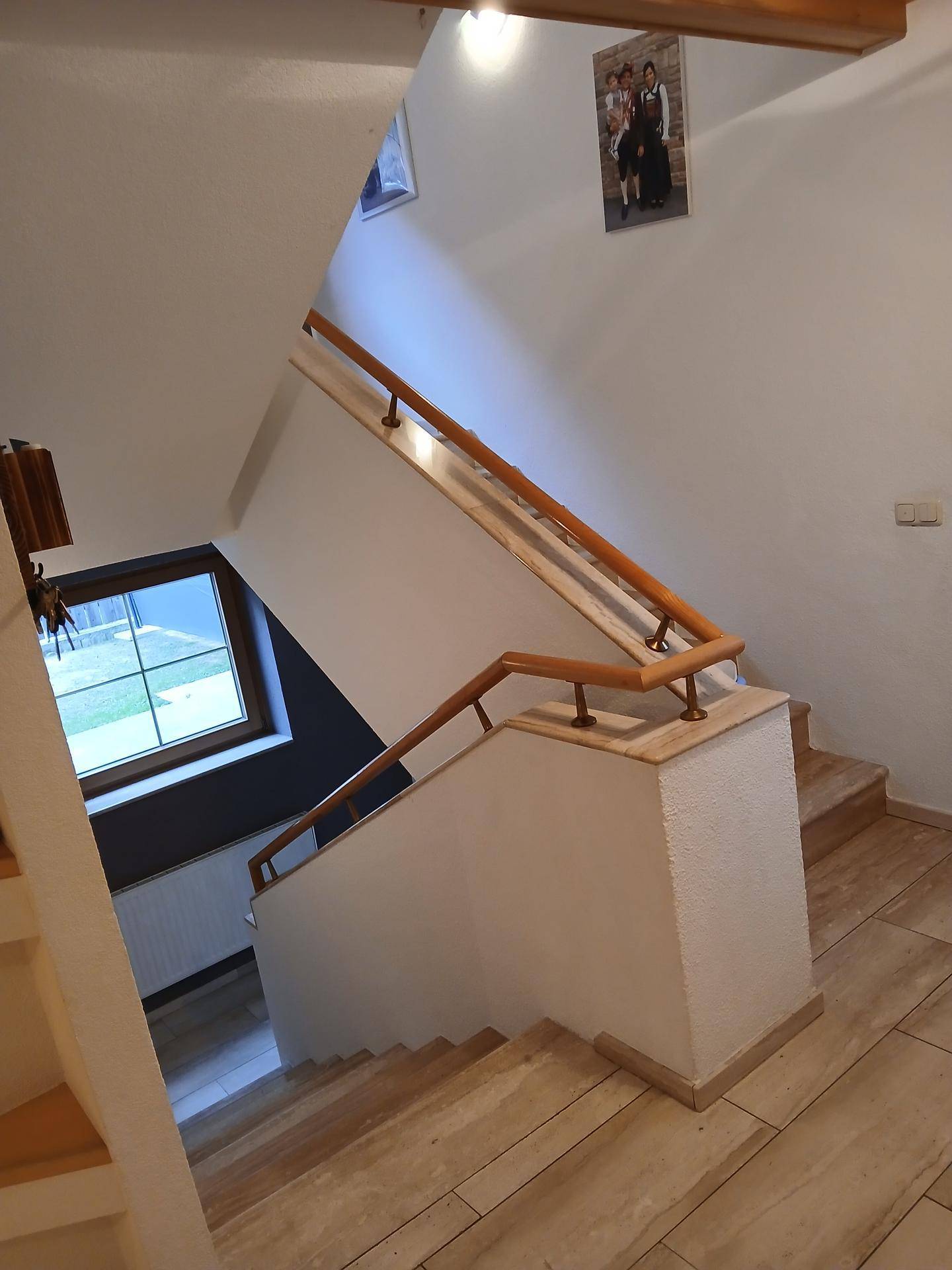 Helles Treppenhaus mit Holzgeländer und gefliesten Stufen, das die Etagen verbindet.