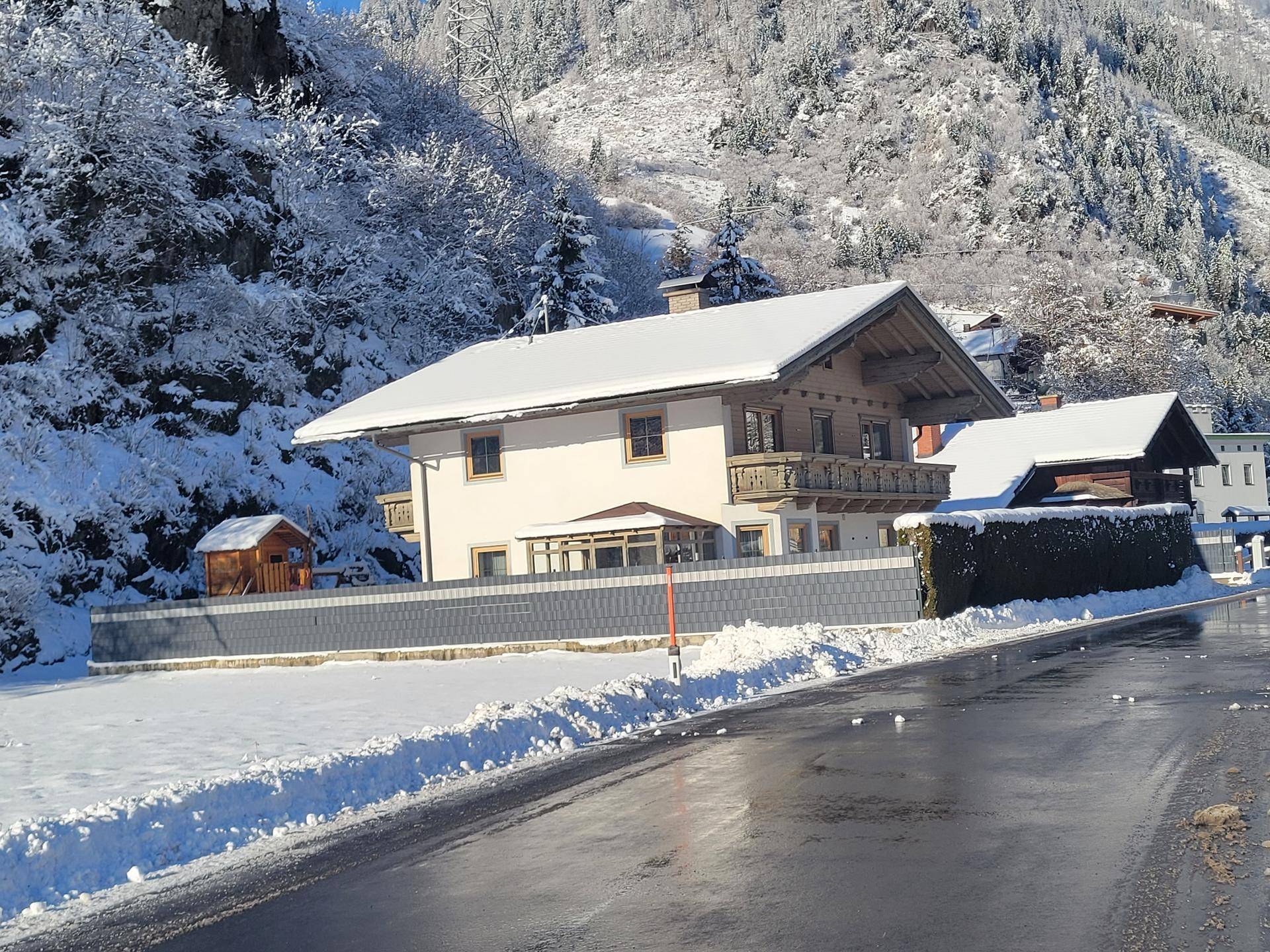 Traditionelles Haus im alpinen Stil mit schneebedecktem Dach und Bergblick im Winter.
