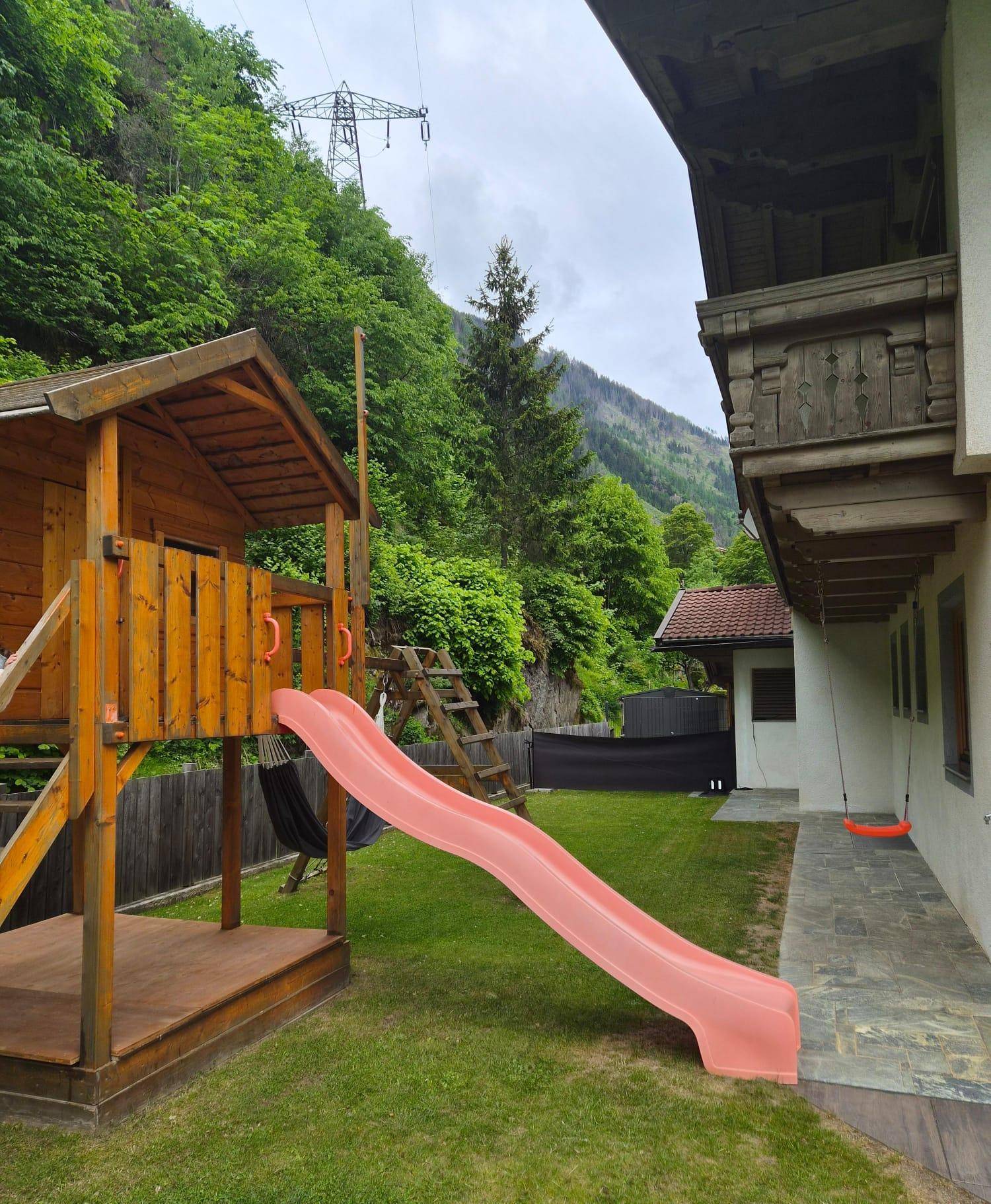 Spielplatz mit Rutsche und Schaukel im Gartenbereich eines Alpenhauses mit Bergblick.