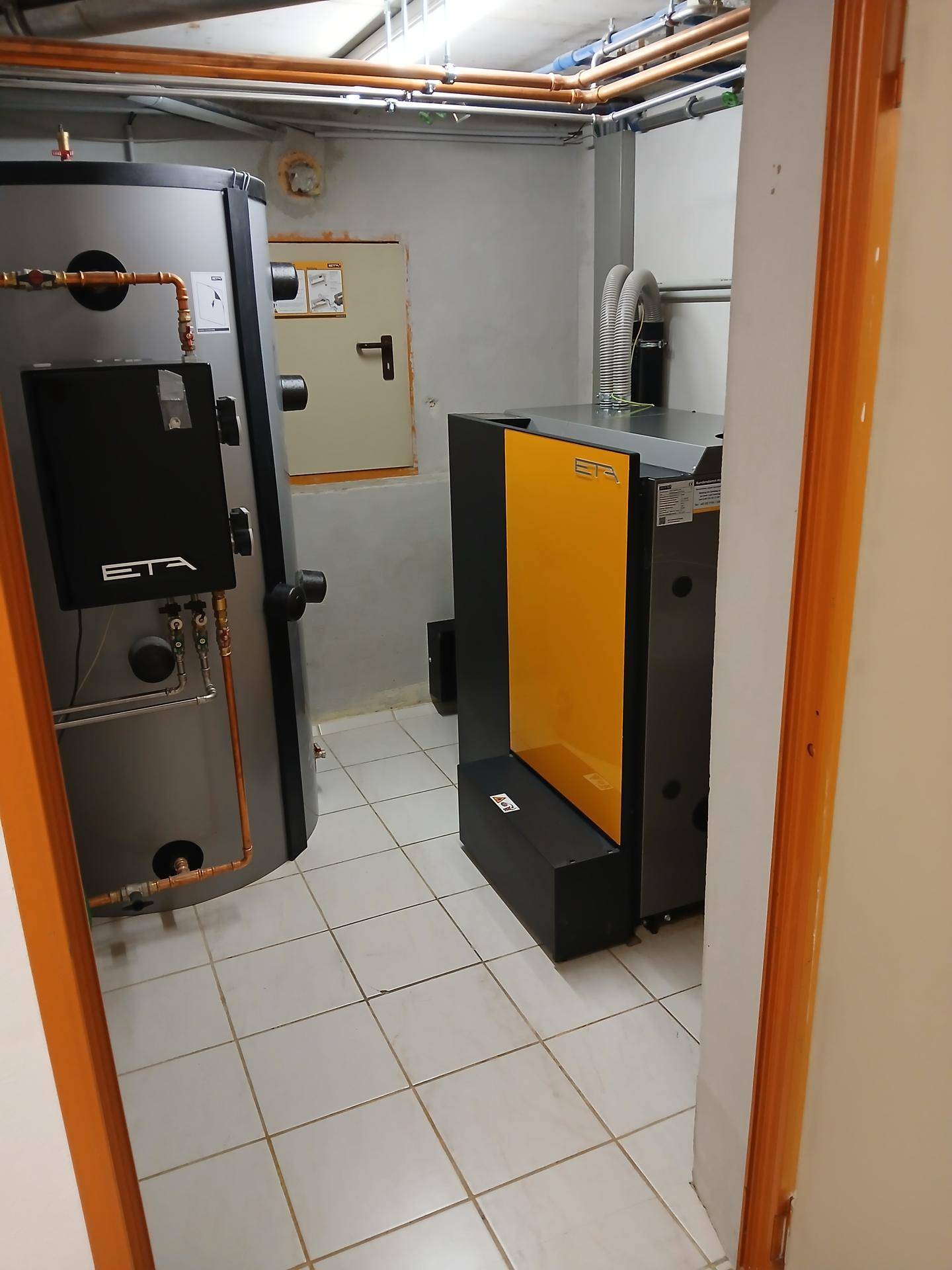 Heizraum mit modernen Heizungsanlagen und Warmwasserspeicher auf Fliesenboden.
