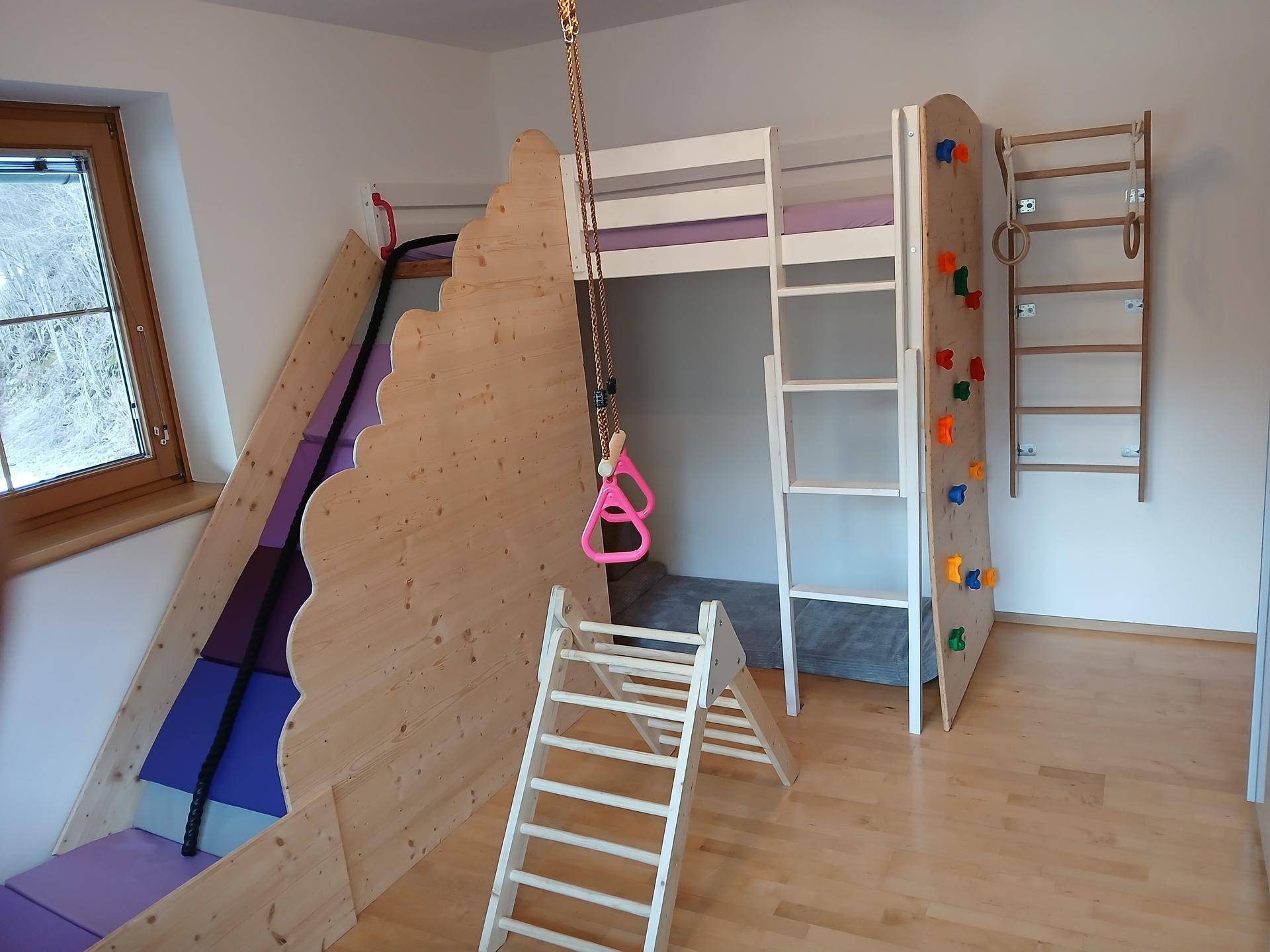 Spielerisches Kinderzimmer mit Hochbett, Rutsche, Kletterwand und Schaukel.