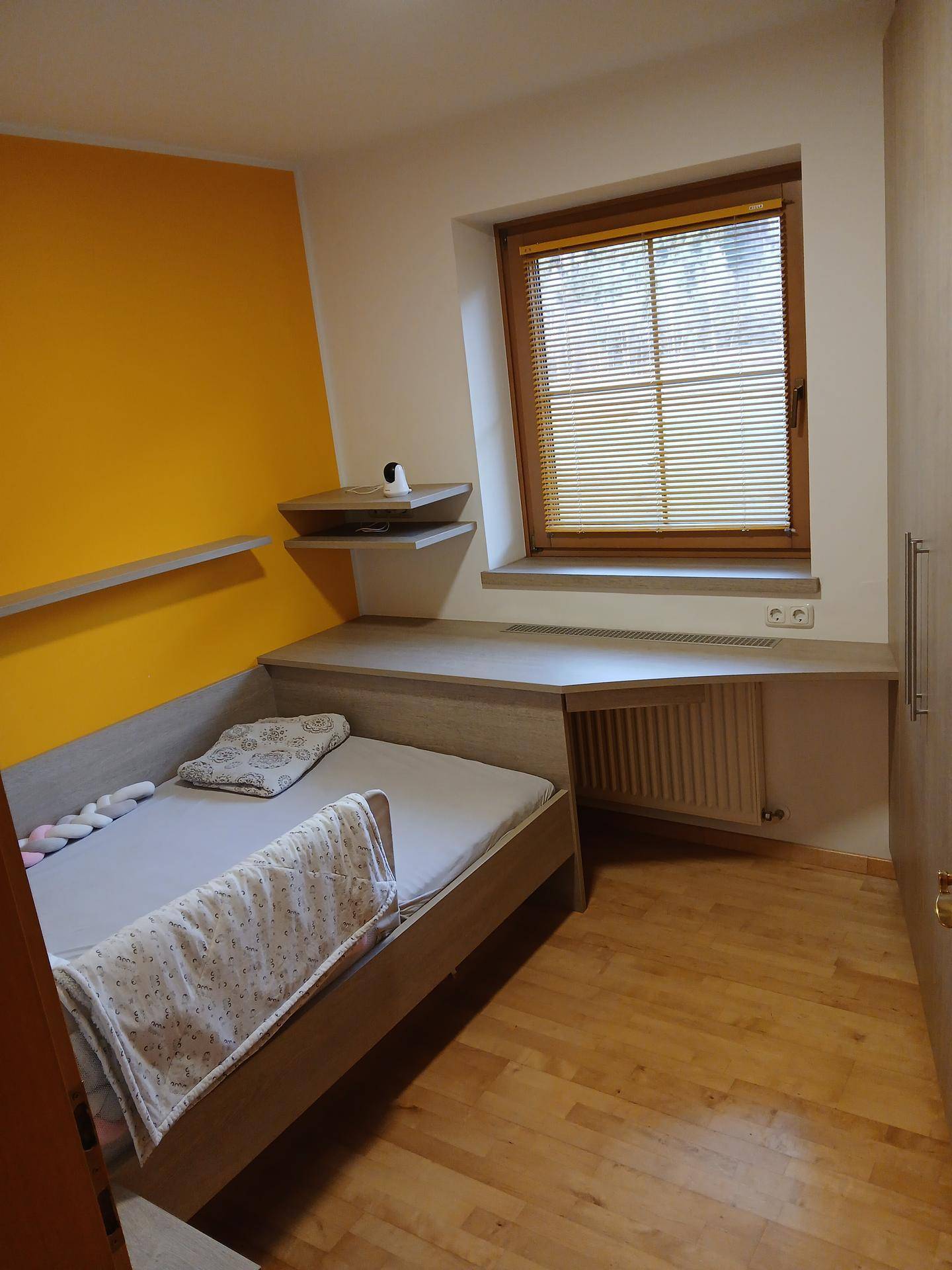 Schlafzimmer mit integriertem Schreibtisch, Bett und gelber Akzentwand.