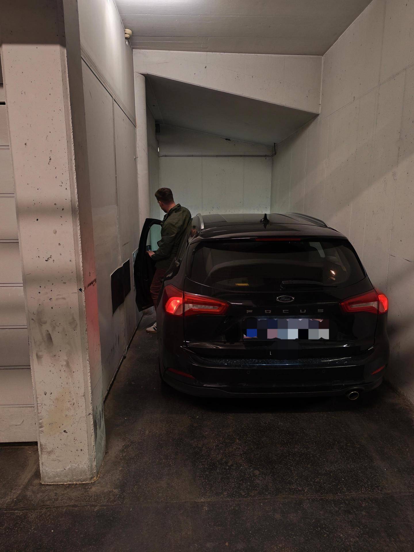 Person steigt aus einem schwarzen Auto in einer Tiefgaragenparklücke mit Betonwänden.