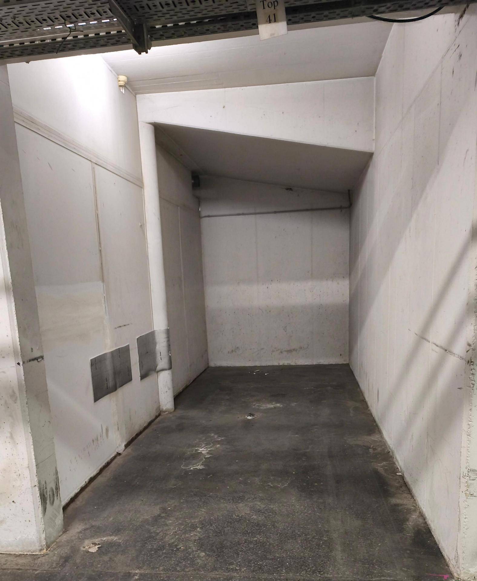 Leere Tiefgaragenparklücke mit Betonwänden und sichtbarer Deckeninstallation für Kabel.