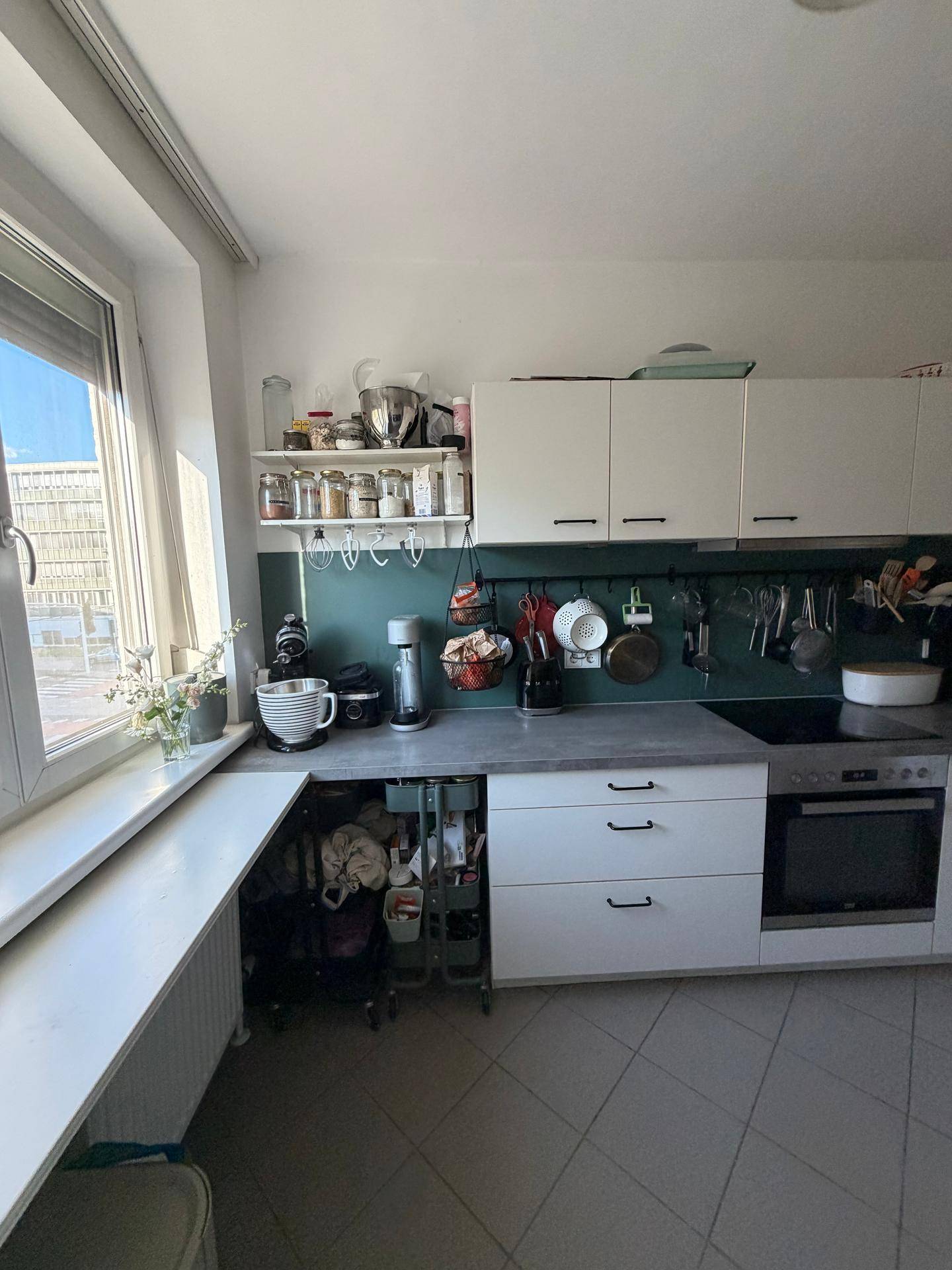 Funktionale Küche mit weißen Schränken, grauer Arbeitsplatte und Fenster.