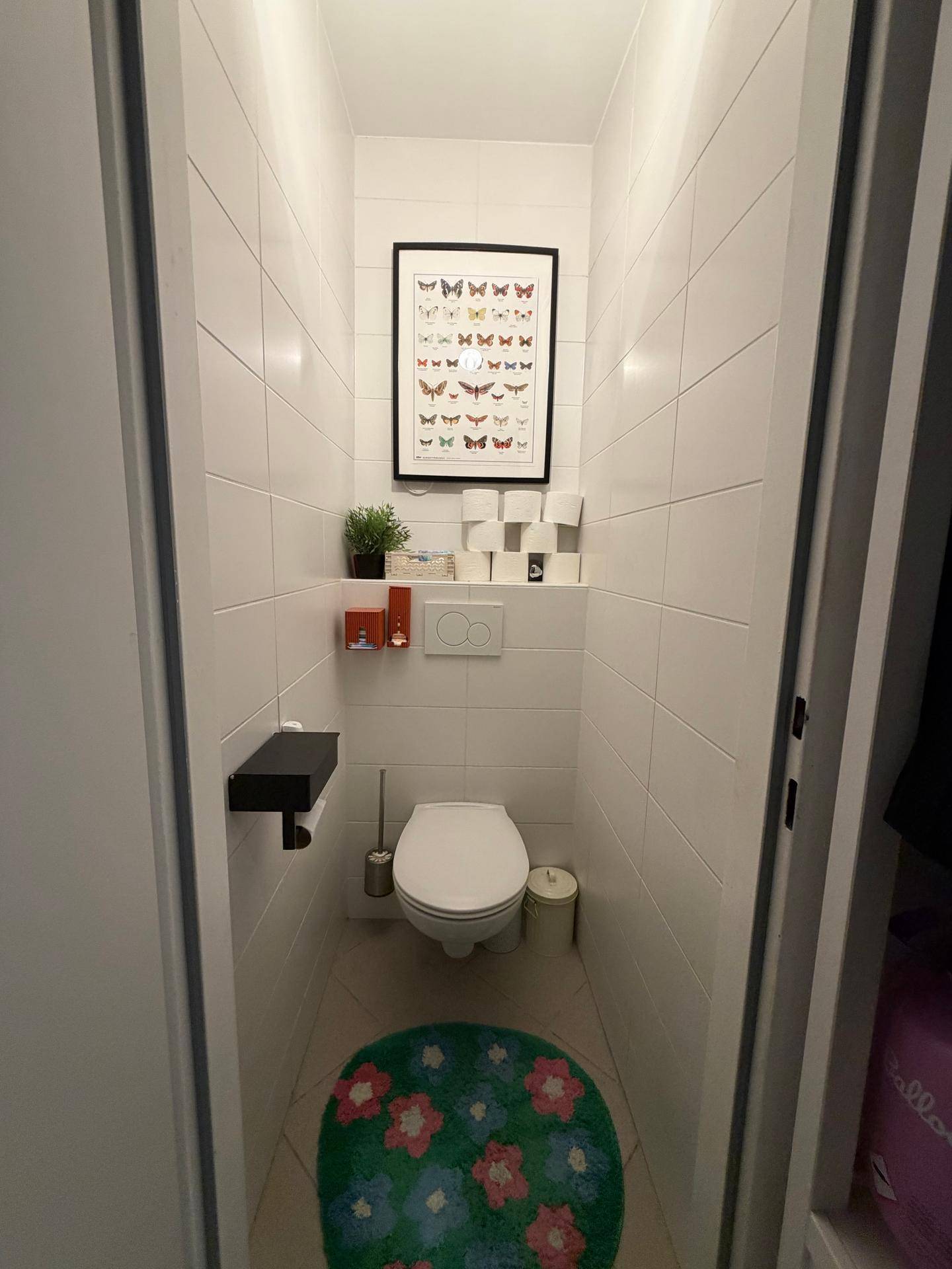 Kleines, funktionales WC mit weißen Fliesen und moderner Toilette.