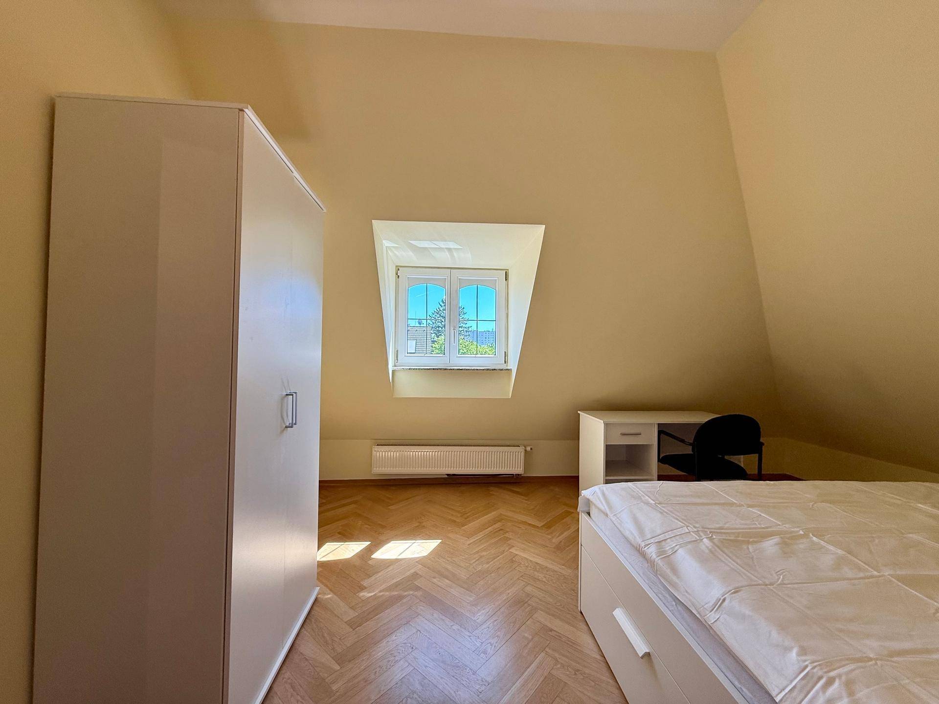 Gemütliches Schlafzimmer im Dachgeschoss mit Schrank, Bett und Schreibtisch, gut beleuchtet.
