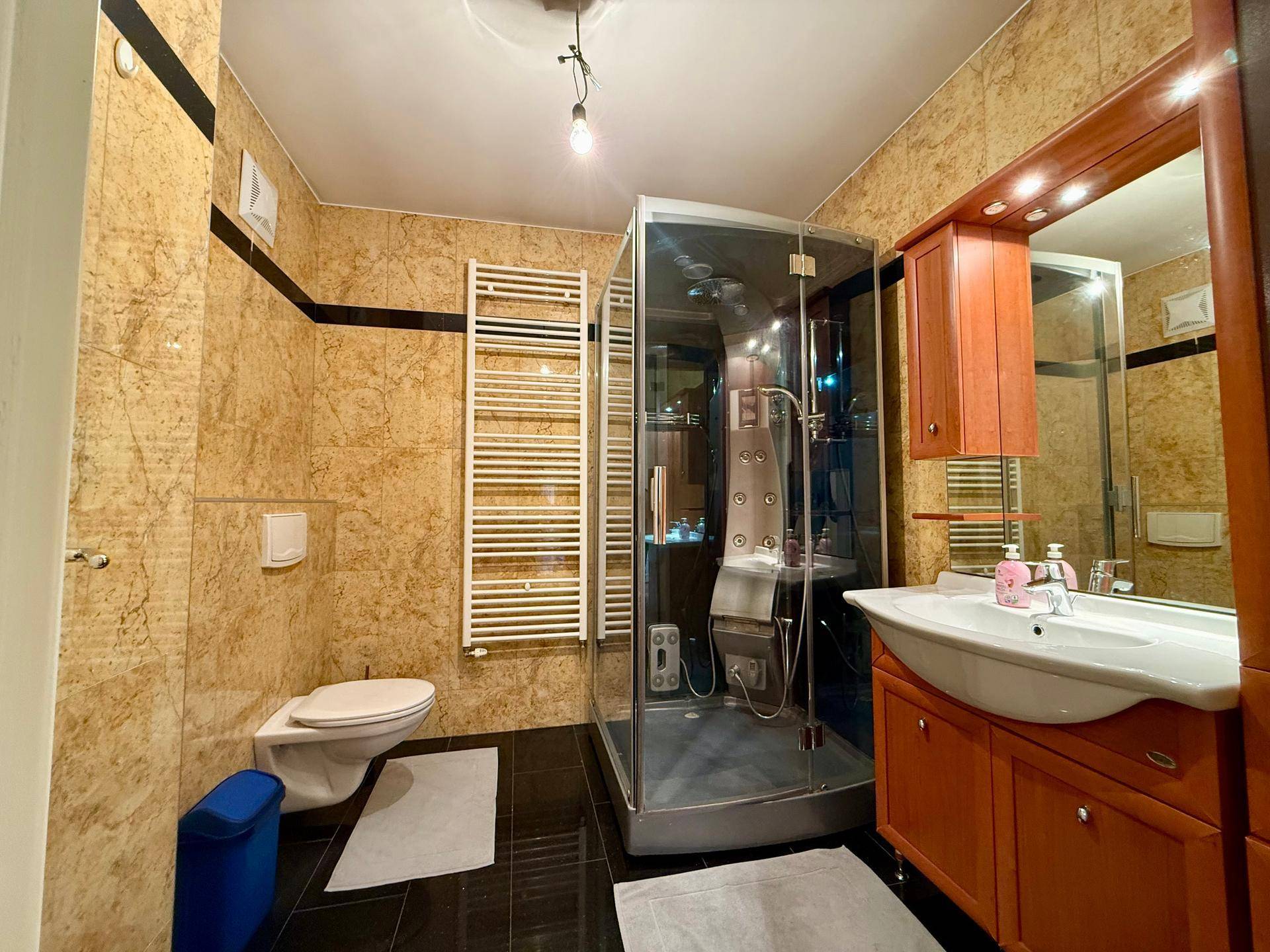 Modernes Badezimmer mit Duschkabine, WC, Waschtisch und beheiztem Handtuchhalter in warmen Farbtönen.