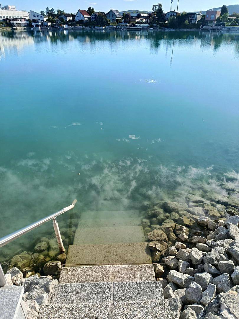 Treppe führt direkt ins klare Wasser des Sees, umgeben von Steinen.