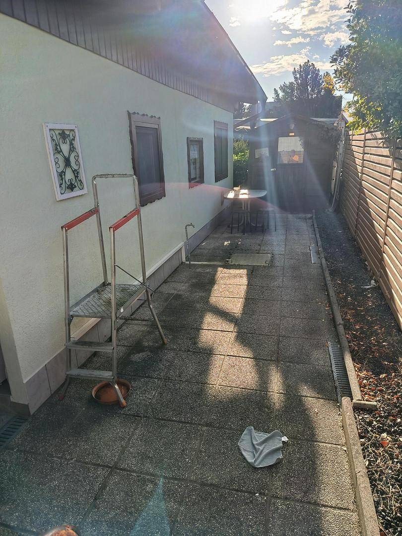 Schmaler gepflasterter Bereich neben dem Haus mit einer Leiter und Sonnenlicht.