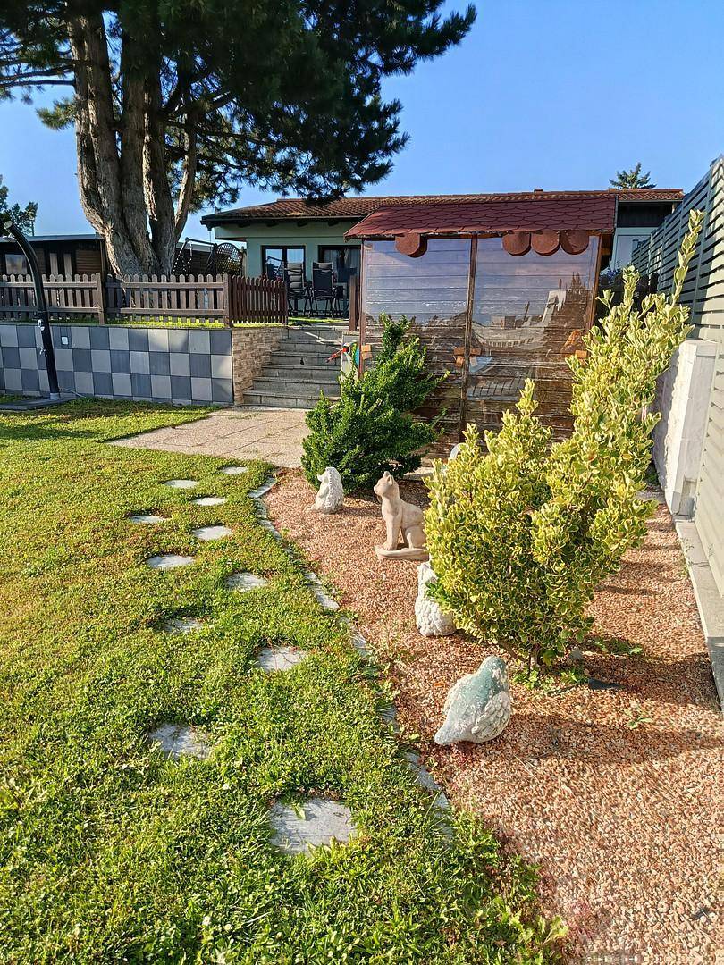 Gartenweg mit dekorativen Elementen und Blick auf das Haus und den See im Hintergrund.
