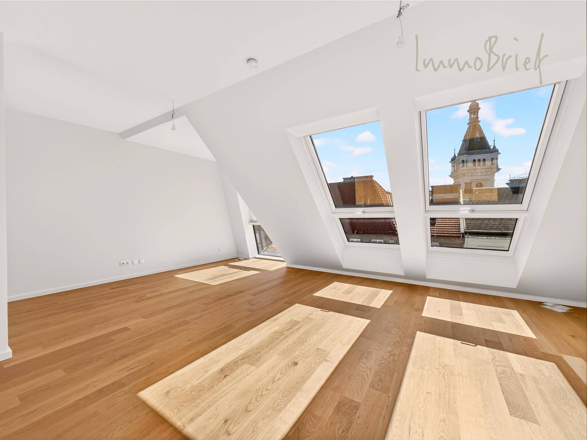 Geräumiger, heller Dachgeschossraum mit Holzboden und mehreren Dachfenstern mit Stadtblick.