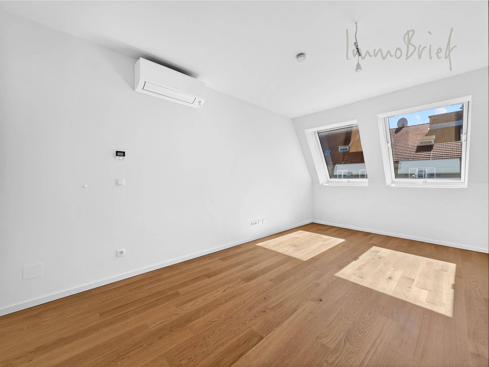 Heller Raum im Dachgeschoss mit Holzboden, Klimaanlage und zwei schrägen Dachfenstern.