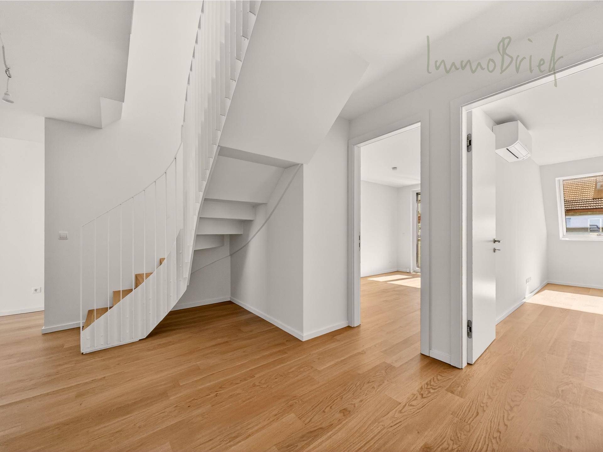 Heller Flur mit moderner Holztreppe und offenen Zugängen zu weiteren Wohnräumen.