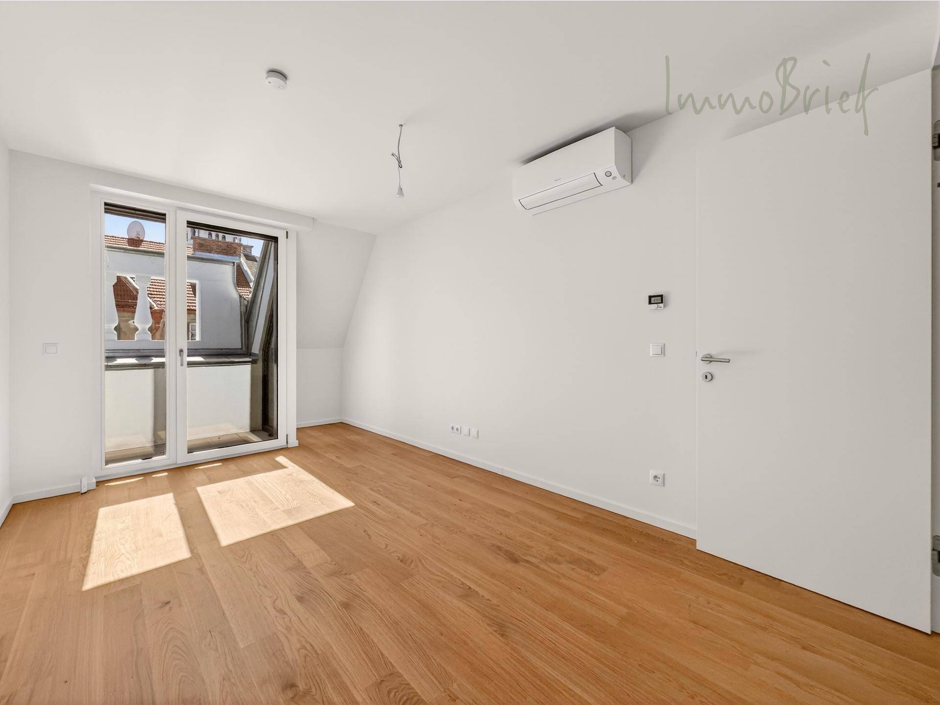 Lichtdurchfluteter, leerer Raum mit Holzboden, Klimaanlage und Zugang zu einem französischen Balkon.