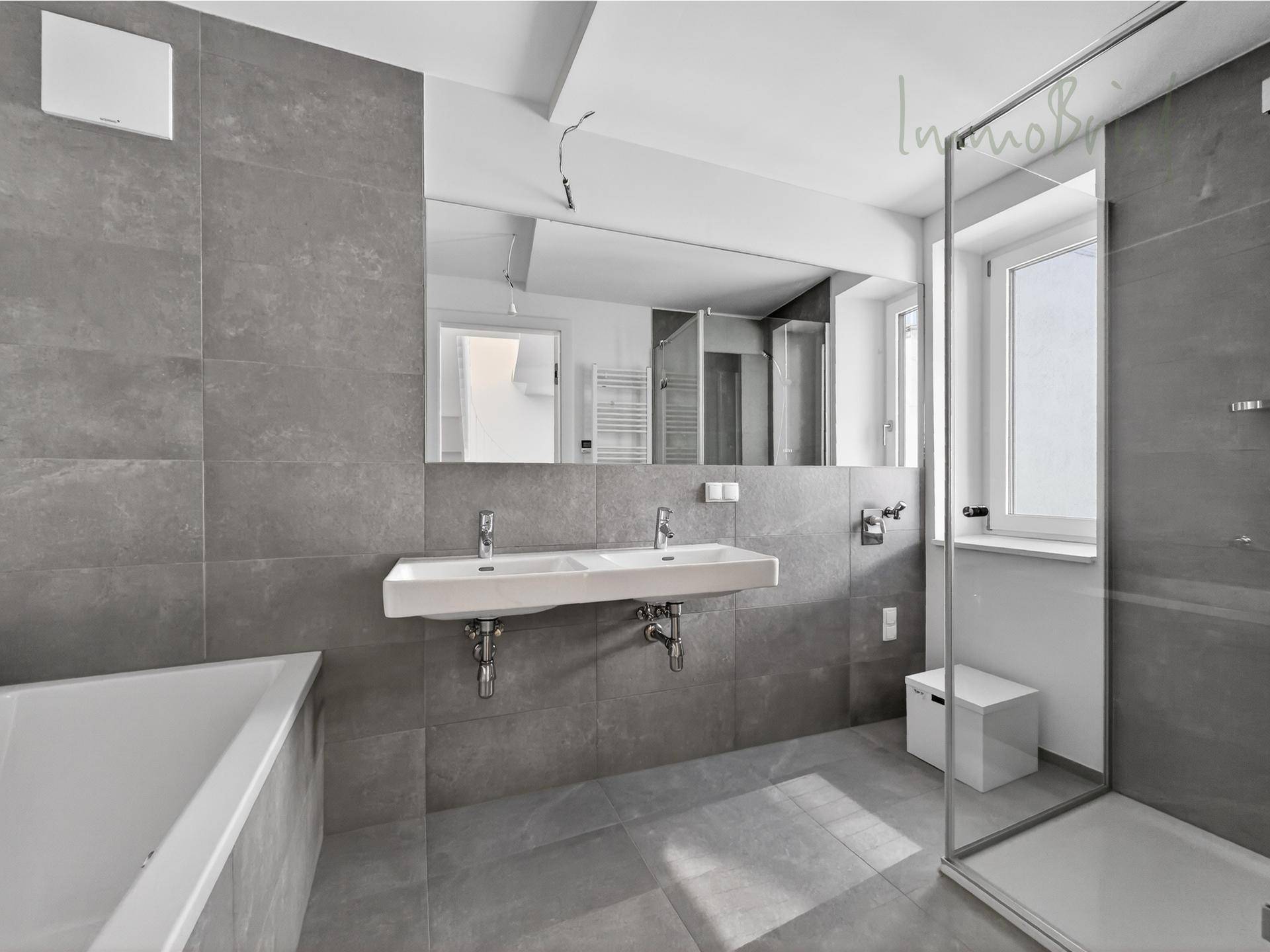 Modernes Badezimmer mit großen grauen Fliesen, Doppelwaschbecken, Badewanne und begehbarer Dusche.