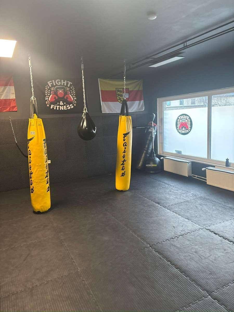 Fitnessraum mit Boxsäcken, Mattenboden und Fenstern, ideal für Kampfsporttraining und körperliche Aktivität.