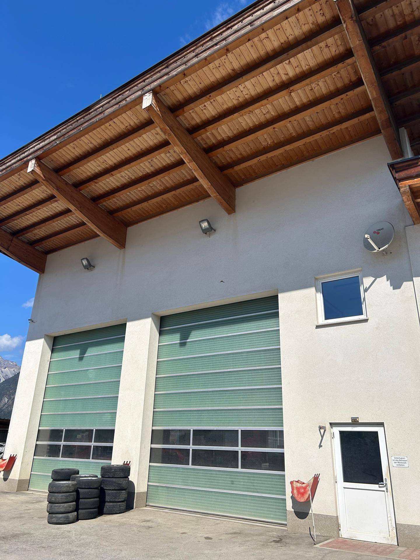 Nahaufnahme der Fassade eines Gewerbegebäudes mit zwei großen Garagentoren und sichtbarer Holzdachkonstruktion.