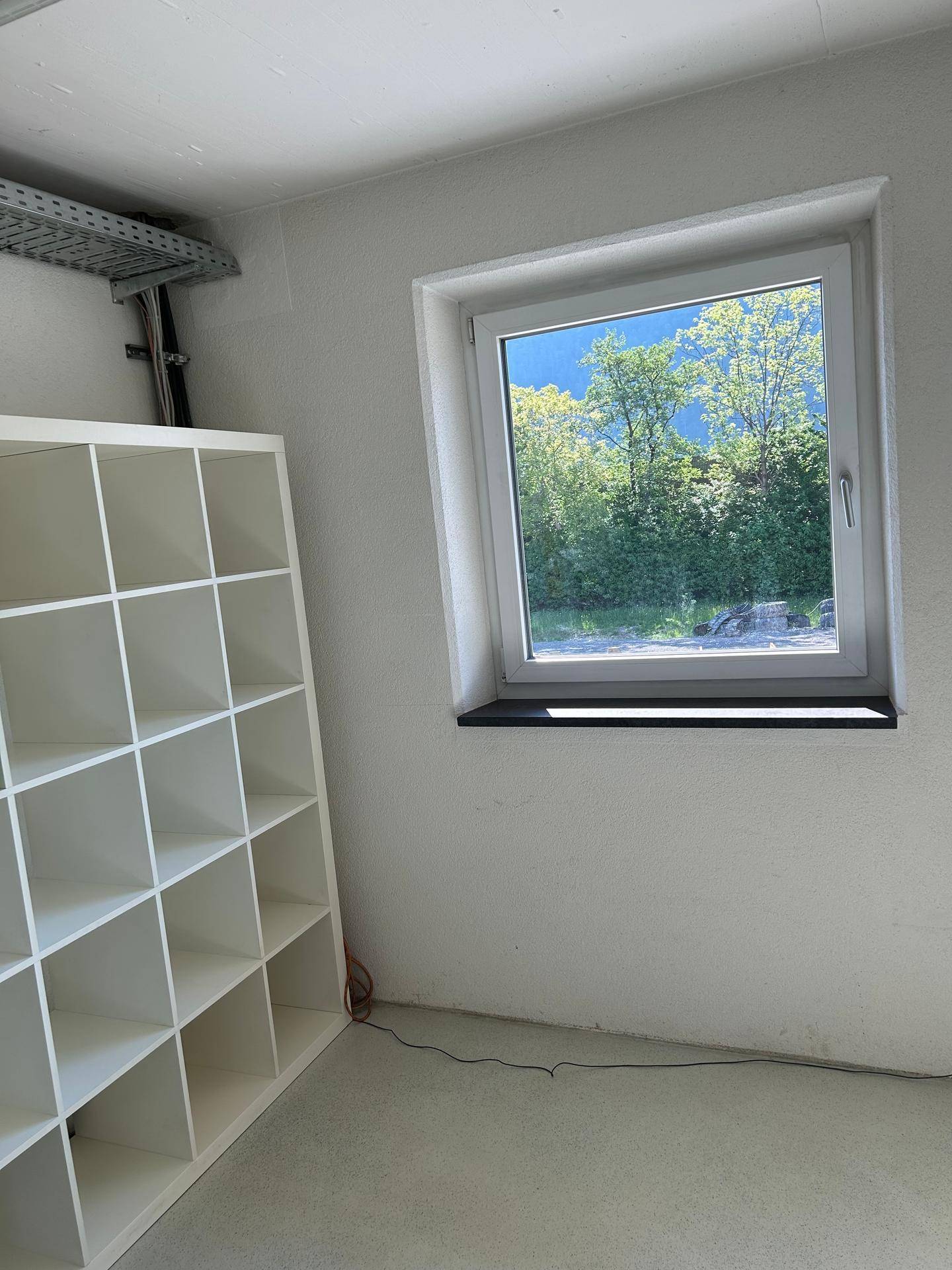Heller Raum mit einem Fenster, das einen grünen Ausblick bietet, und einem weißen Regal.