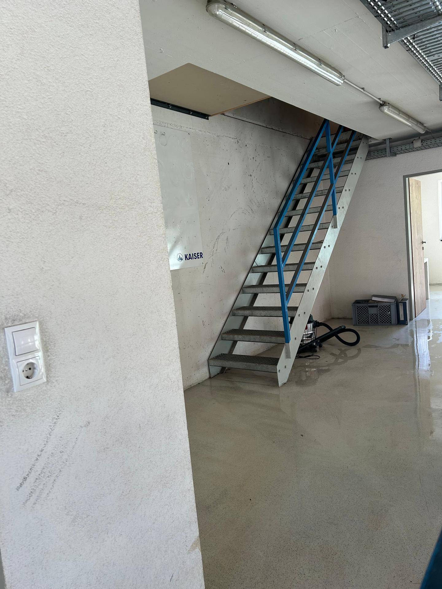 Treppenaufgang mit blauen Geländern in einem hellen Raum mit Betonboden.