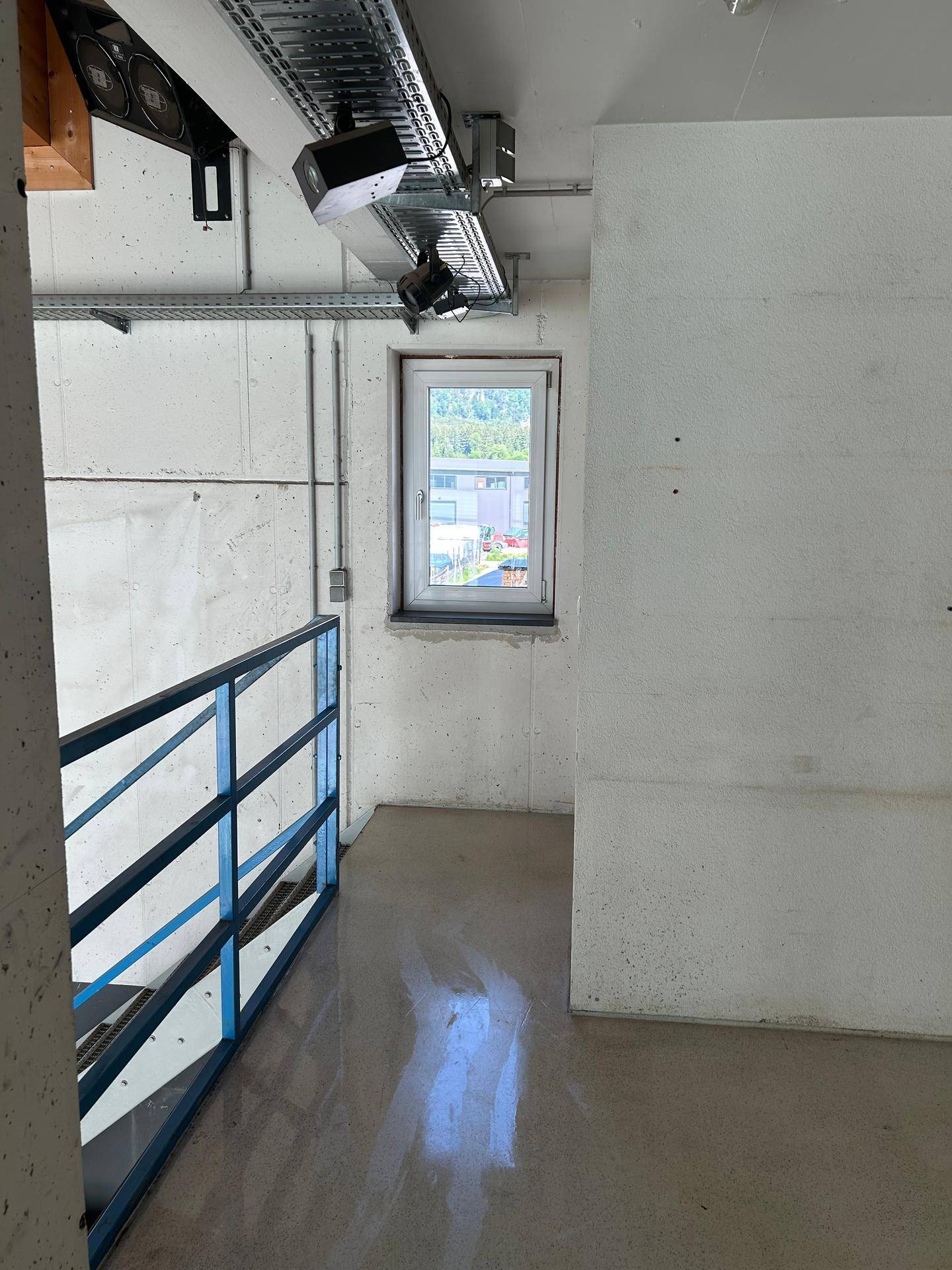 Flur im Obergeschoss mit einem Fenster und Blick auf die Umgebung, neben einer blauen Treppe.
