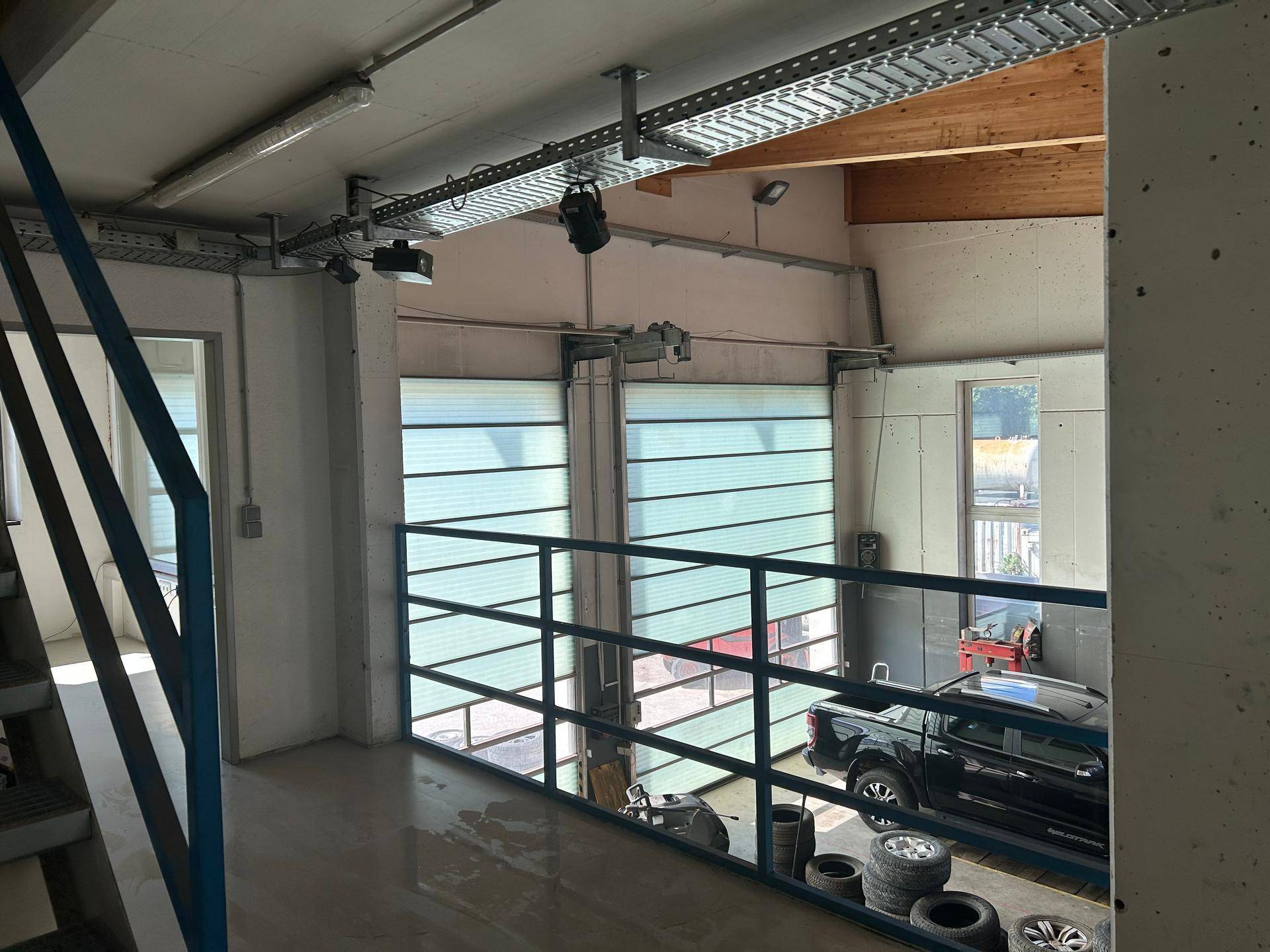 Blick von der Galerie auf die Garagentore und den unteren Werkstattbereich mit einem geparkten Fahrzeug.