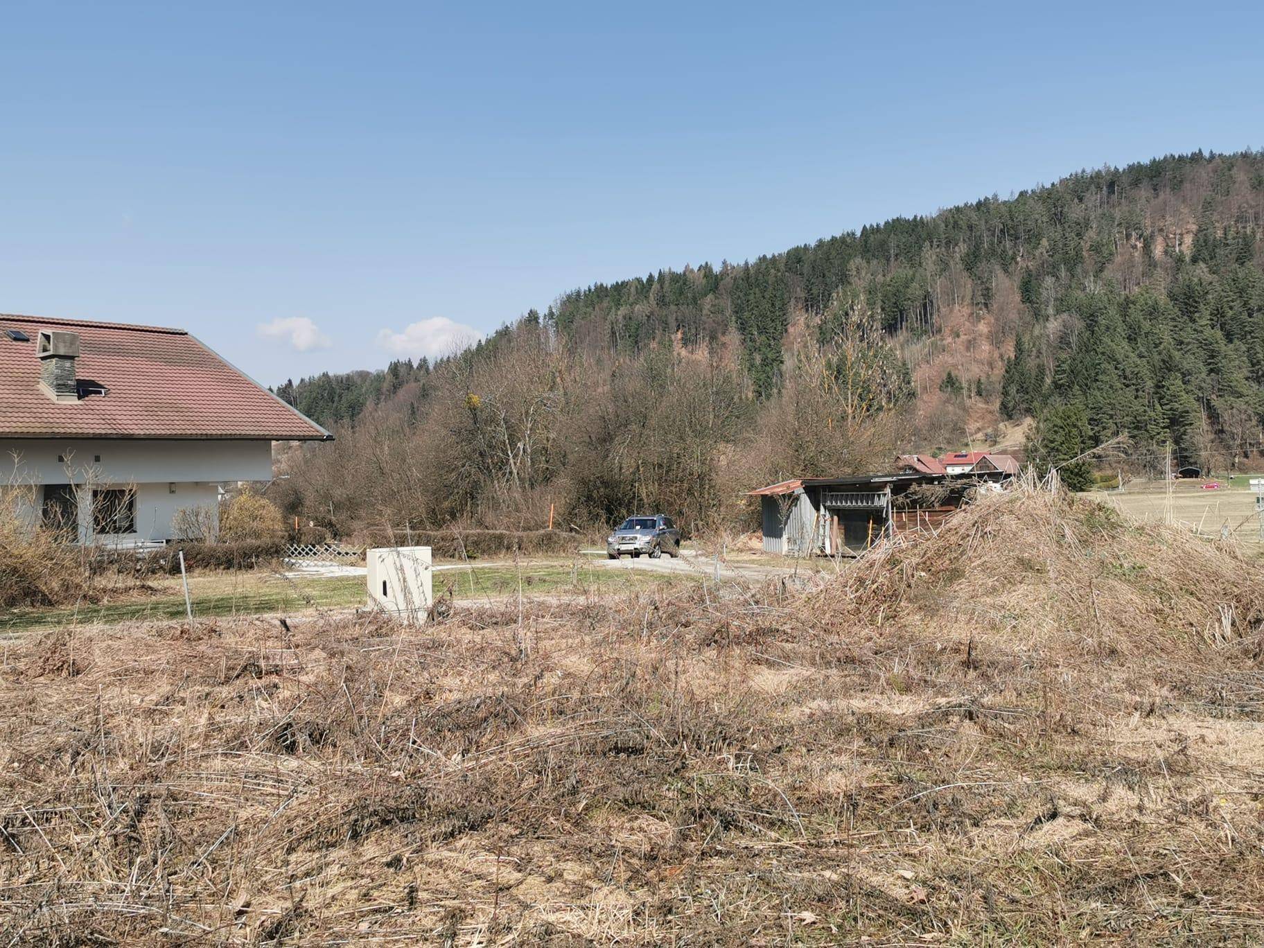 Weitläufiges Gelände mit einem Haus und einem Auto im Hintergrund, umgeben von bewaldeten Hügeln.