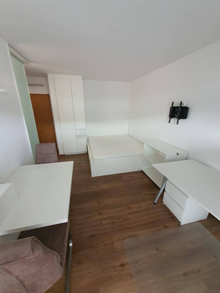 Geräumiges Studioapartment mit Schlafbereich, Kleiderschrank und zwei Arbeitsplätzen auf Laminatboden.