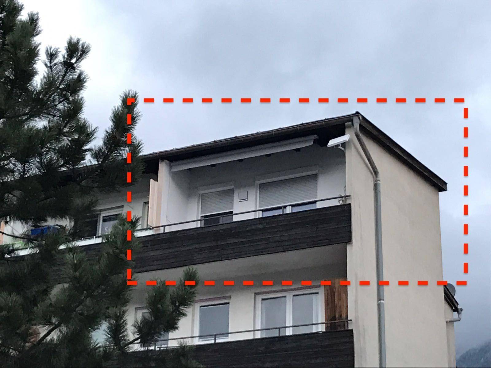 Außenansicht eines Mehrfamilienhauses mit Balkonen und Bäumen im Vordergrund unter bewölktem Himmel.
