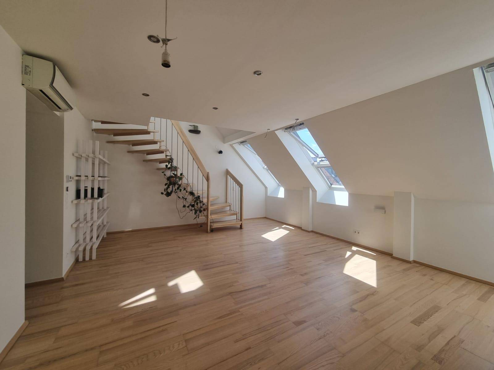 Heller und geräumiger Wohnbereich mit Holztreppe, Dachfenstern und Klimaanlage im Dachgeschoss.