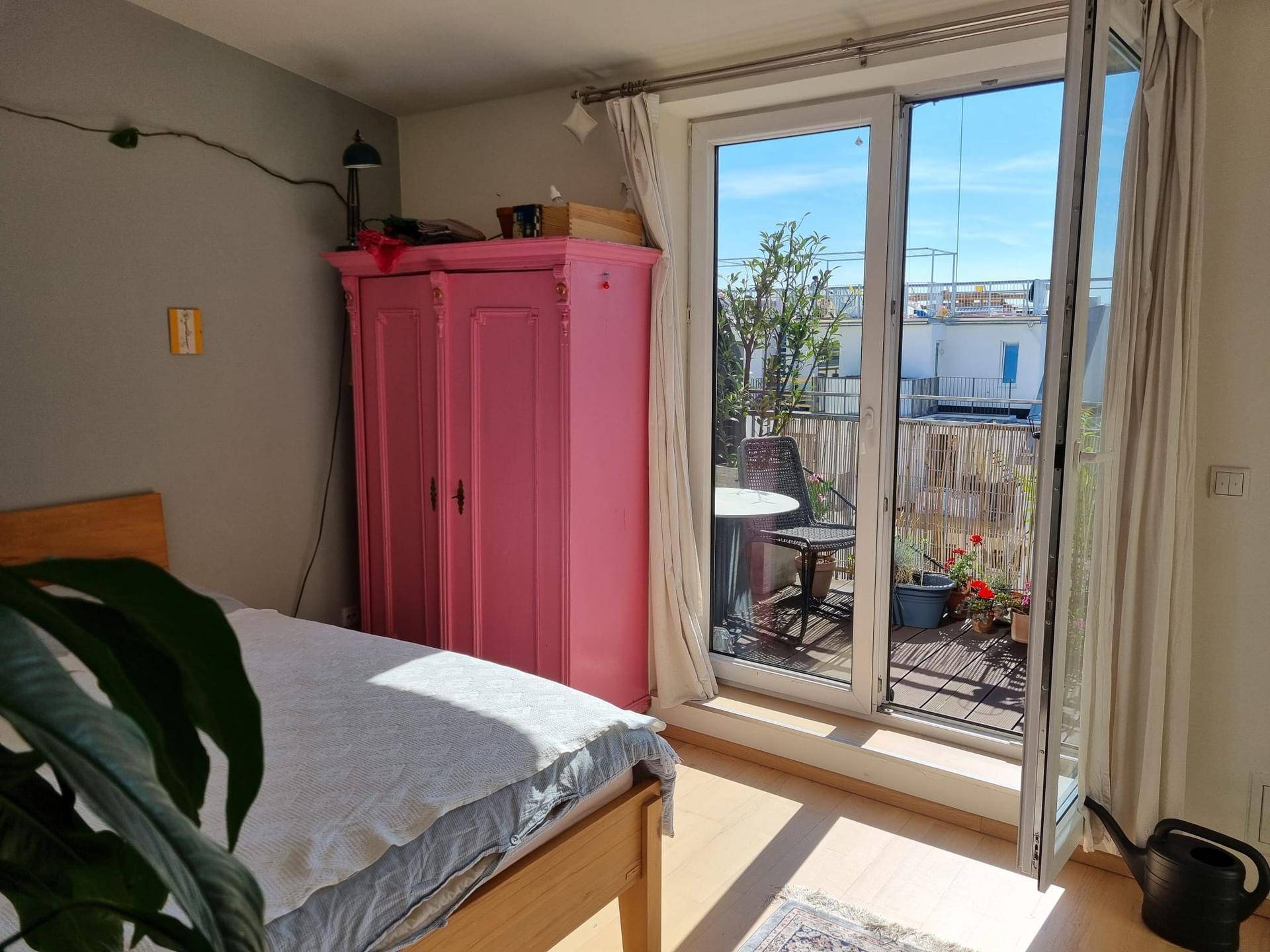Schlafzimmer mit Holzbett und Zugang zu einer sonnigen Terrasse mit Sitzgelegenheiten.