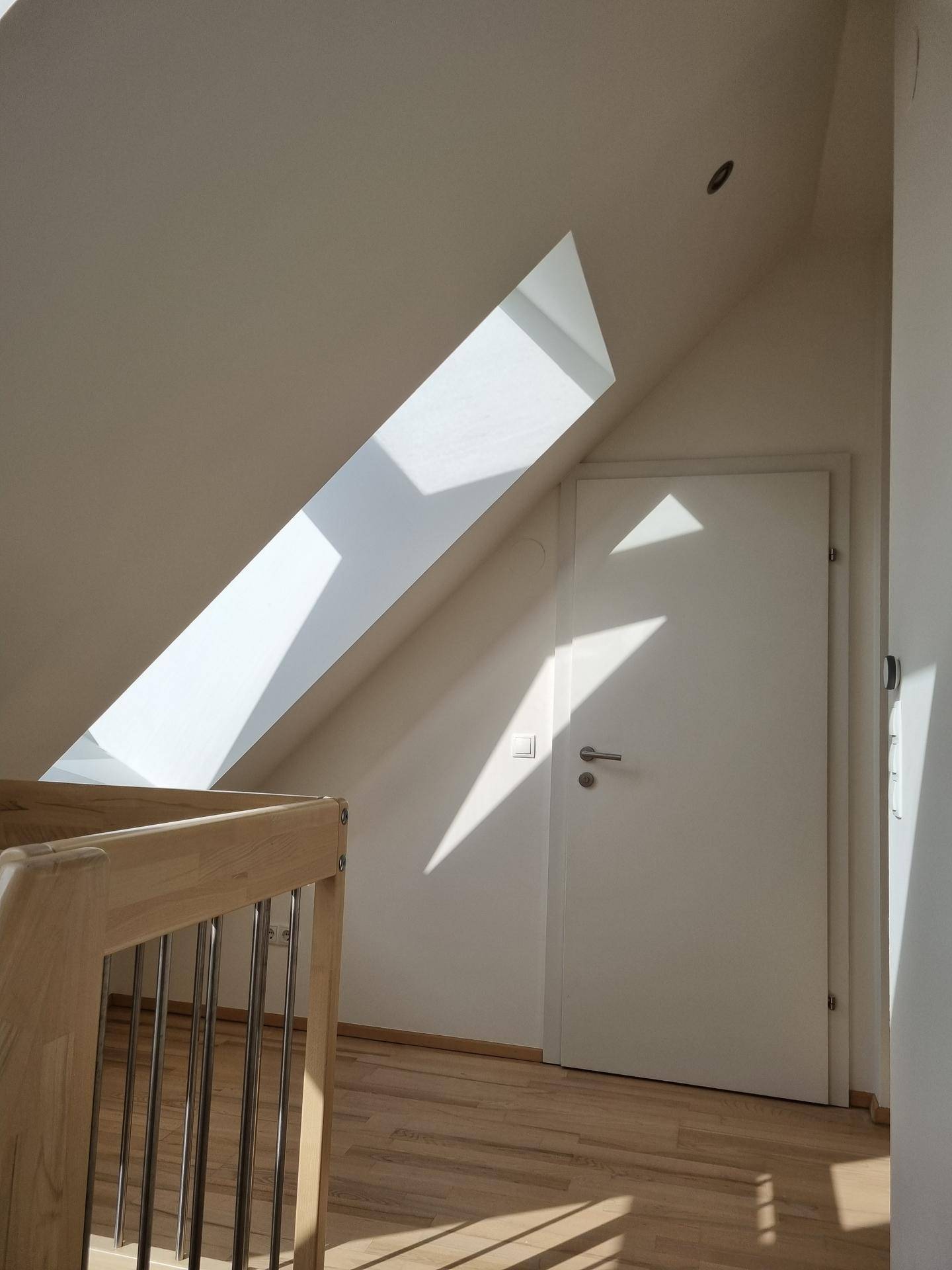Heller Flurbereich mit Holzboden, Tür und einem Dachfenster, das Licht hereinlässt.