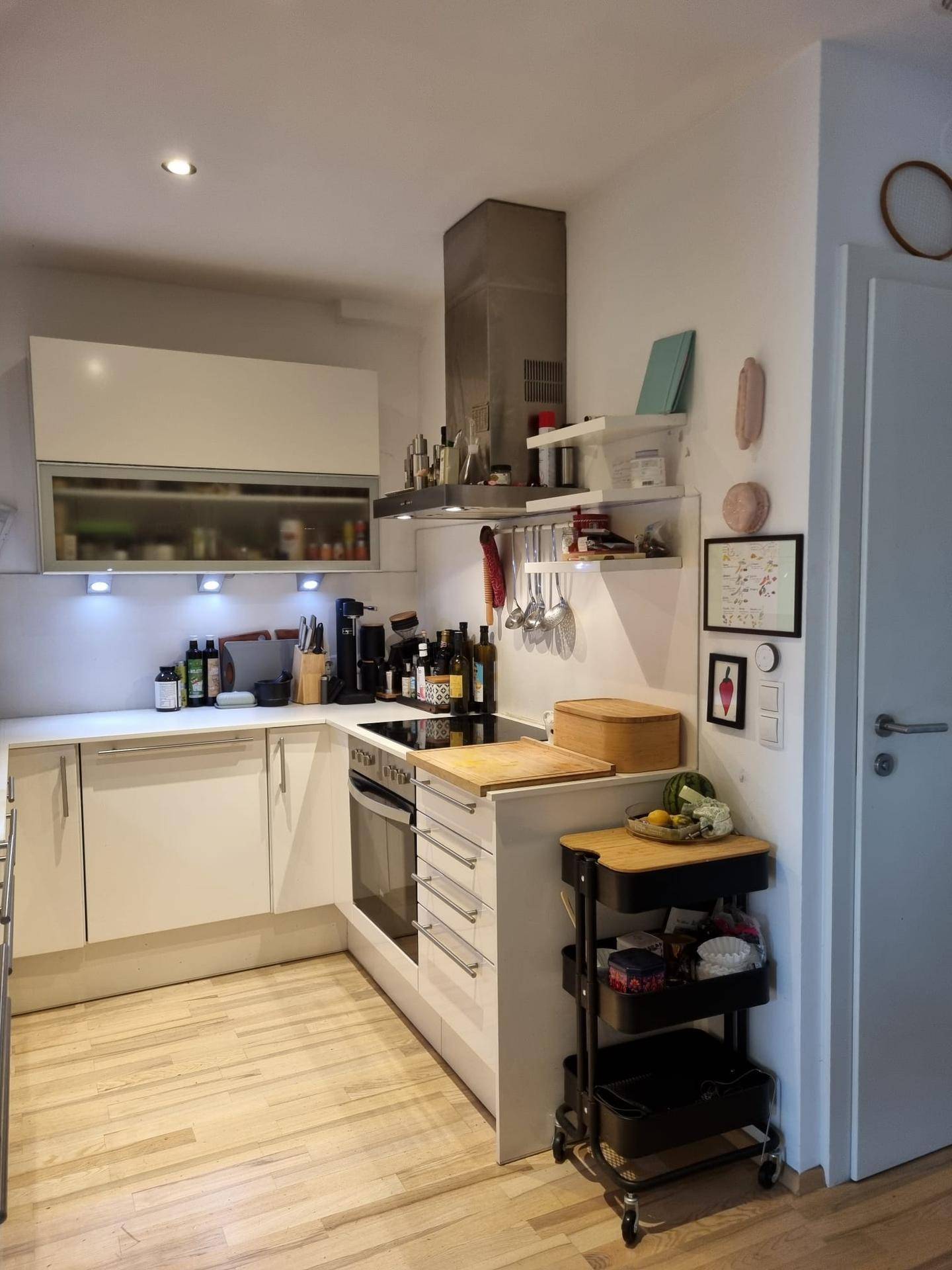 Moderne Küche mit weißen Hochglanzschränken, integriertem Backofen und Dunstabzugshaube.