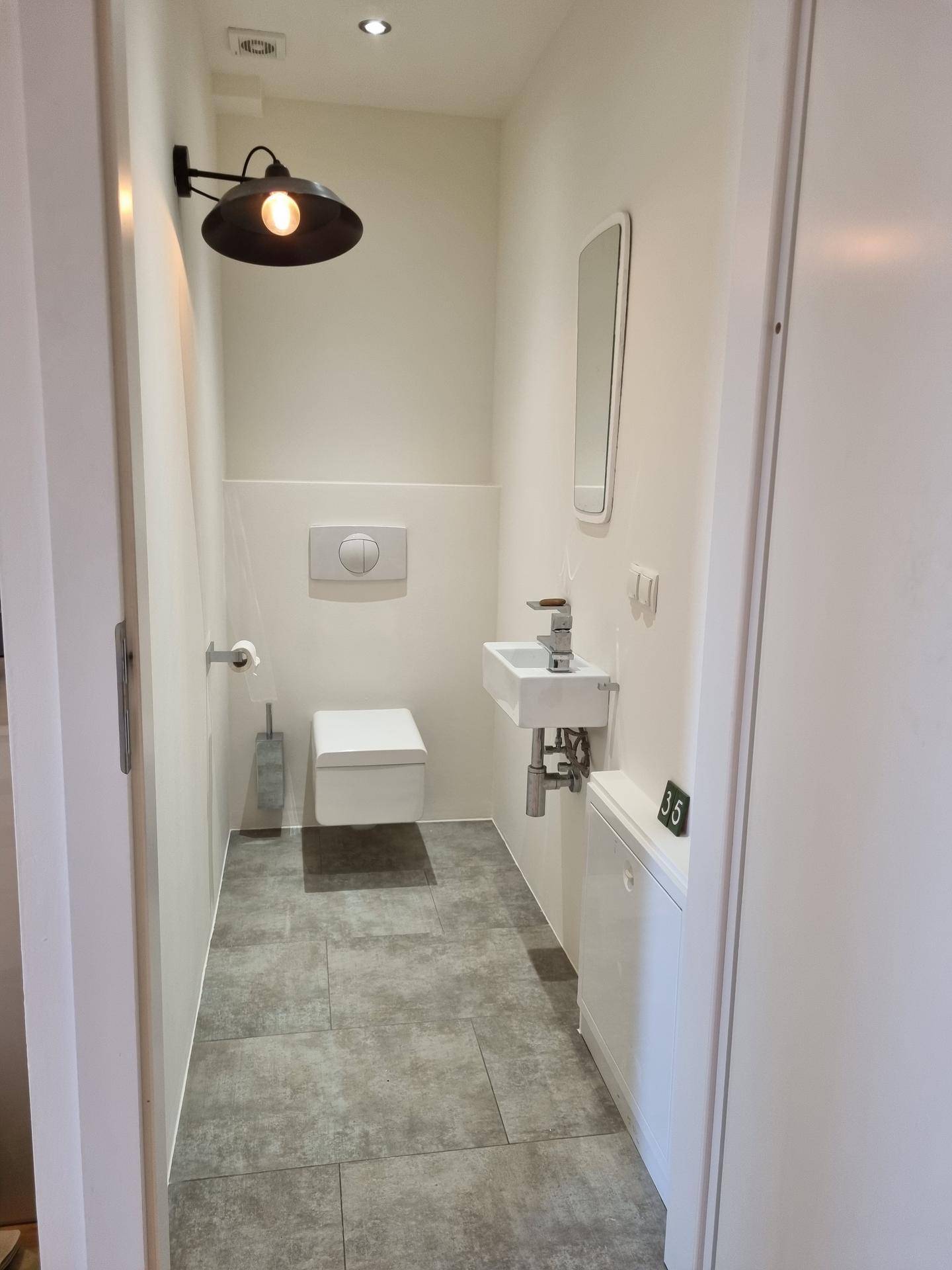 Kleines, modernes Gäste-WC mit Wand-WC, Waschbecken und dunklen Fliesen.