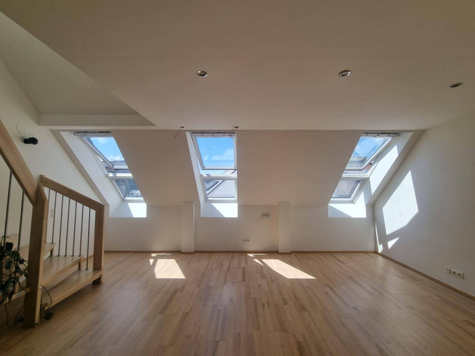 Weitläufiger Dachgeschossraum mit drei großen Dachfenstern, die viel Tageslicht hereinlassen.