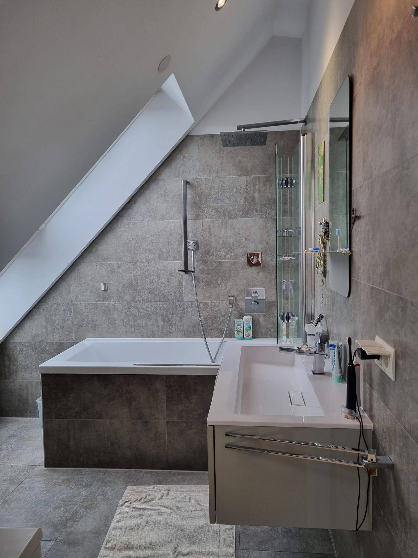 Modernes Badezimmer mit Badewanne, Duschbereich und Waschtisch unter einer Dachschräge.