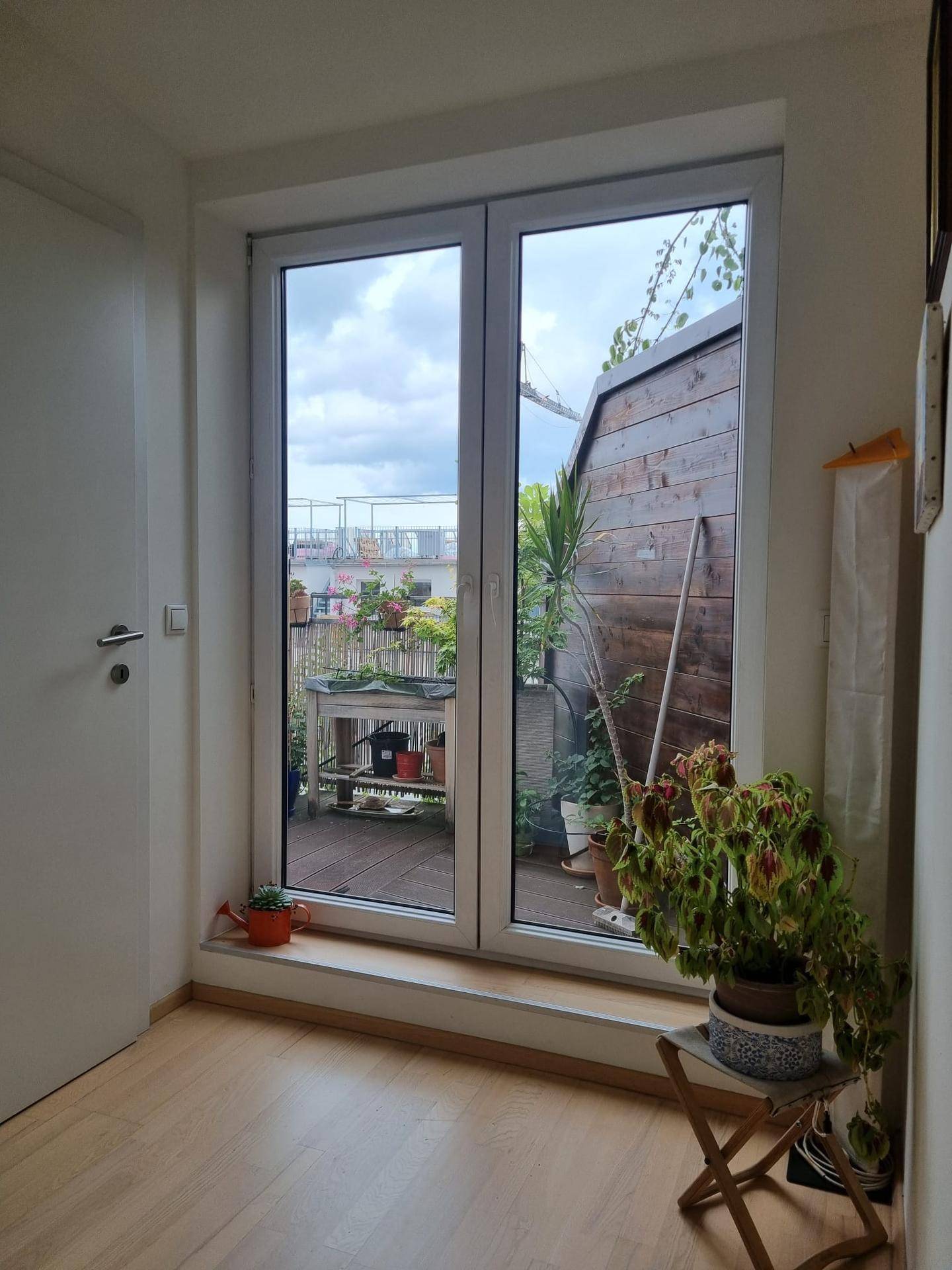 Glastür, die den Zugang zu einer bepflanzten Dachterrasse mit Holzboden ermöglicht.