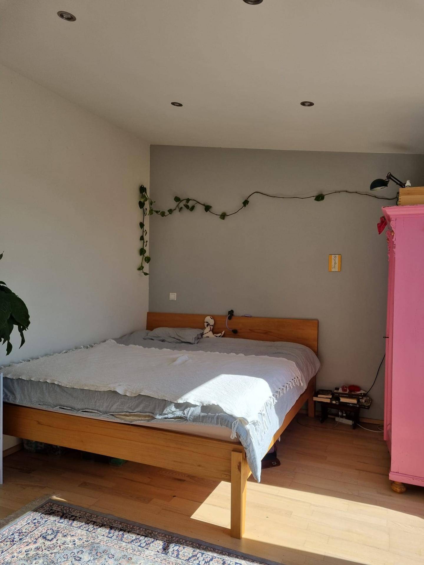Helles Schlafzimmer mit Holzbett, rosa Kleiderschrank und Teppich, durchflutet von Sonnenlicht.