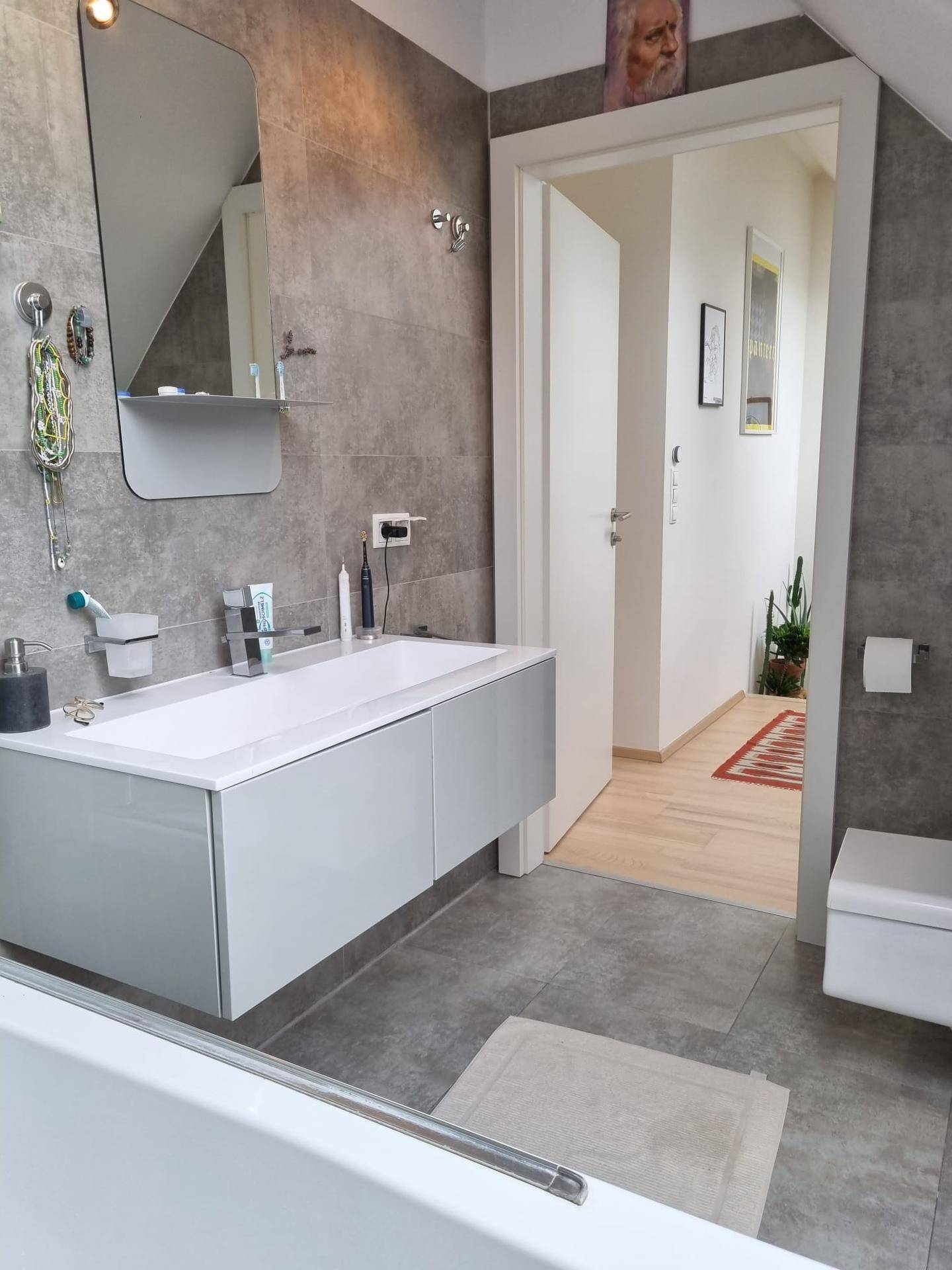 Modernes Badezimmer mit Waschtisch, Spiegel und Toilette, mit Blick in den angrenzenden Flur.