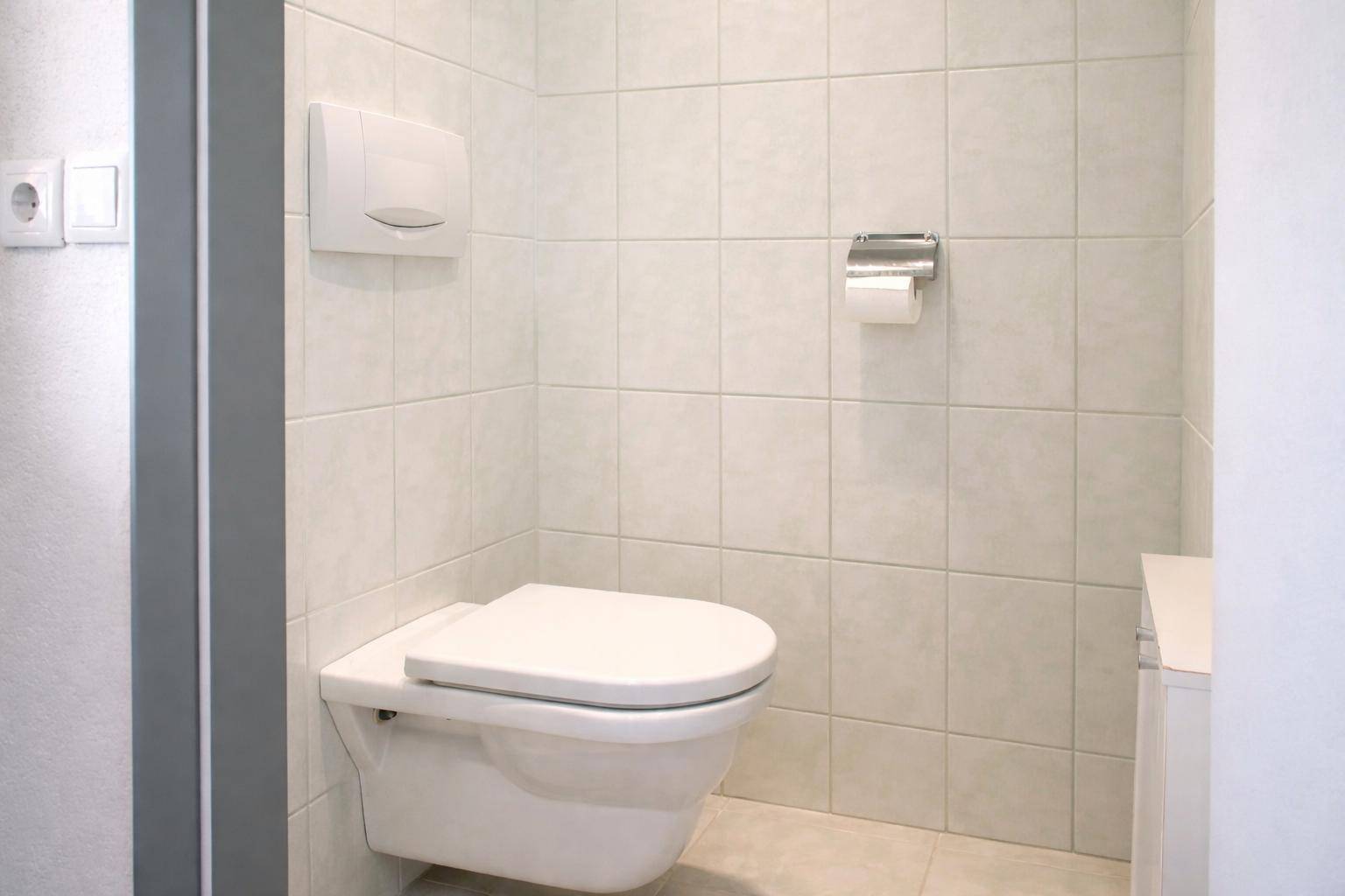 Kleines WC mit wandhängender Toilette und hellen Fliesen an Wänden und Boden.