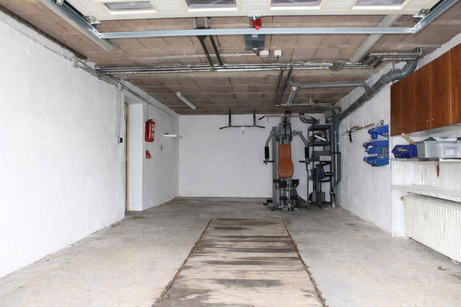 Geräumige Garage mit Fitnessgeräten, Regalen und Zugang zum Haus.