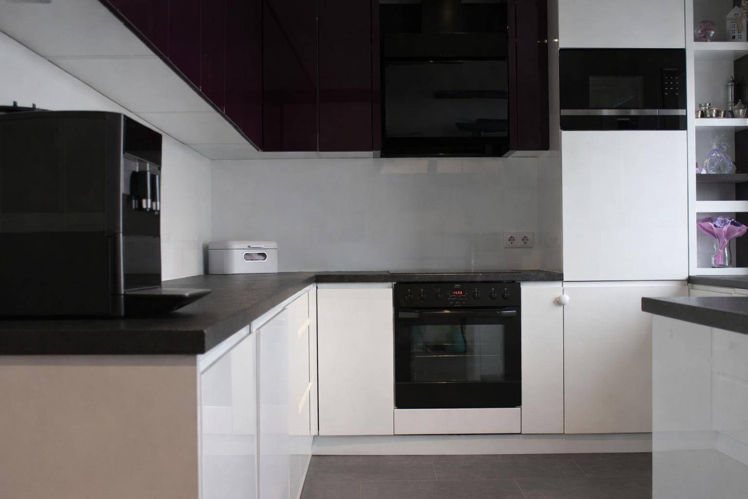 Moderne Küche mit weißen und dunklen Hochglanzfronten, Backofen und Dunstabzugshaube.