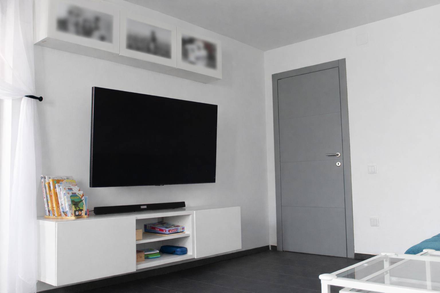 Wohnzimmerbereich mit großem Wandfernseher, weißem TV-Möbel und grauer Tür.