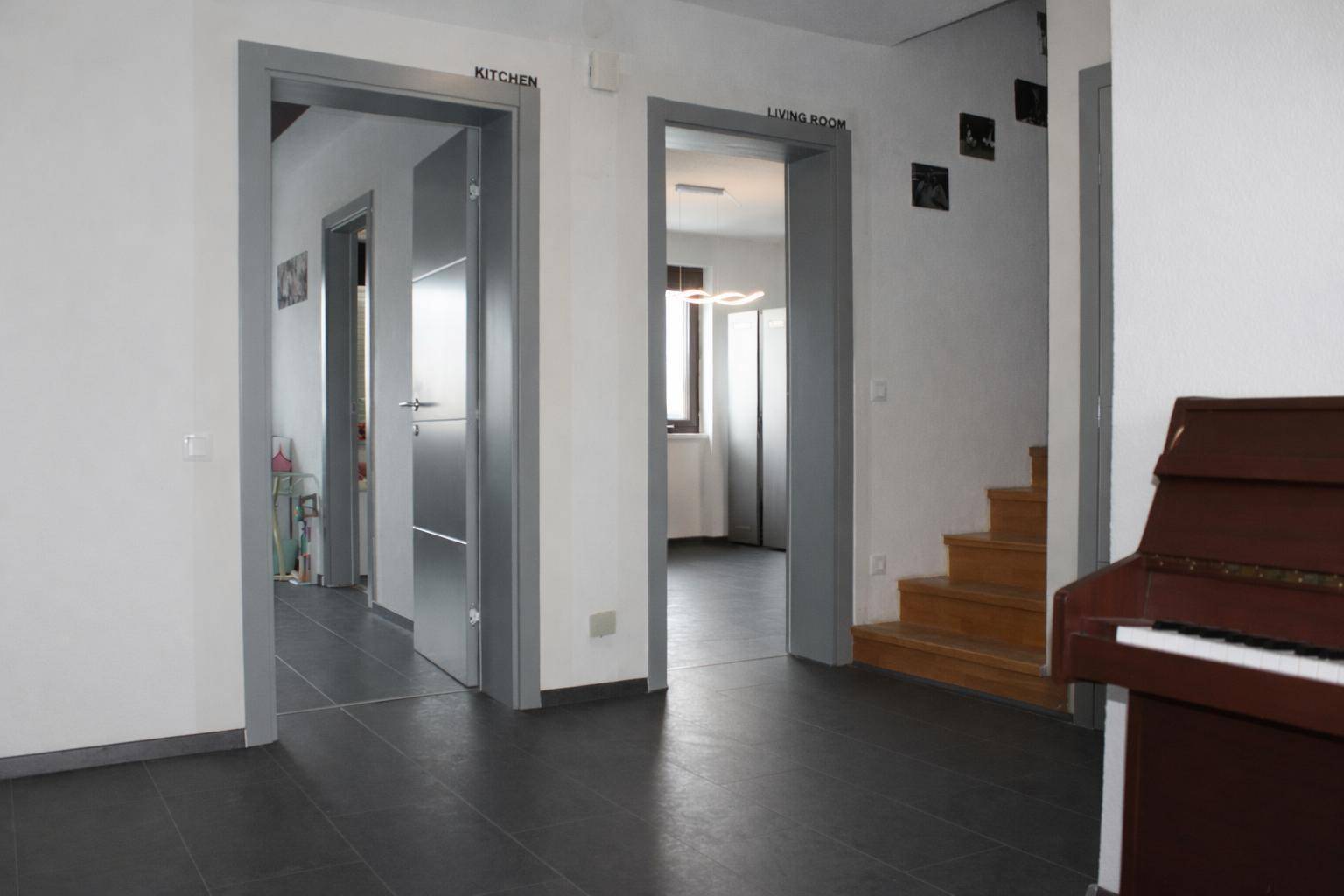 Heller Flur mit dunklem Fliesenboden, Holztreppe und Türen zu Küche und Wohnzimmer.
