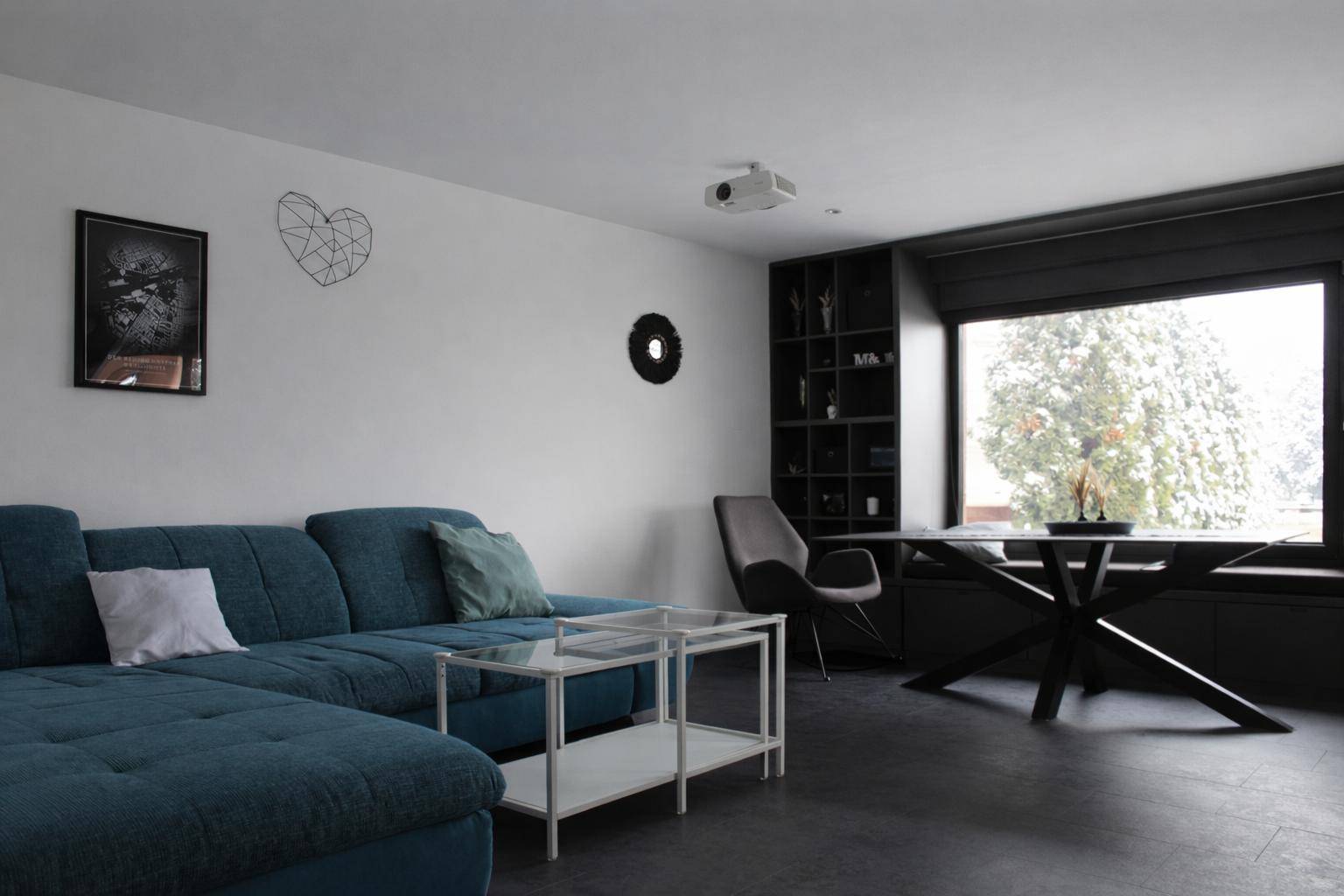 Modernes Wohnzimmer mit blauem Ecksofa, dunklem Boden und großem Fenster.